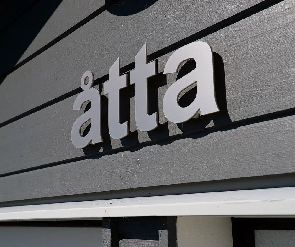 Bokstavsskylt "åtta" i rostfritt stål på grå träfasad