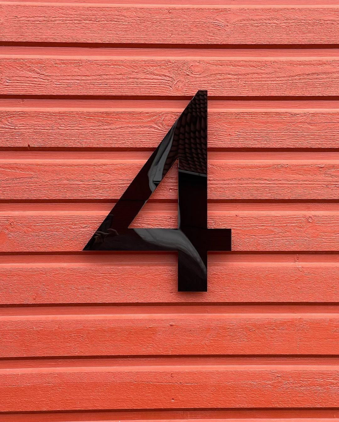 Husnummer 4 i svart akryl på röd trävägg
