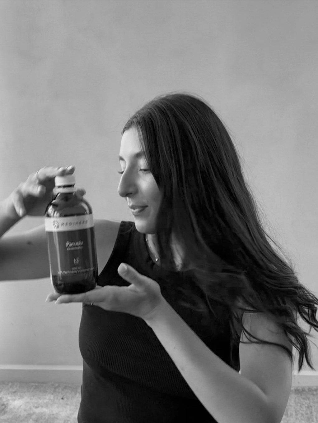 A woman with long dark hair holding a herbal tincture bottle to the left of her, in a black and white photograph.