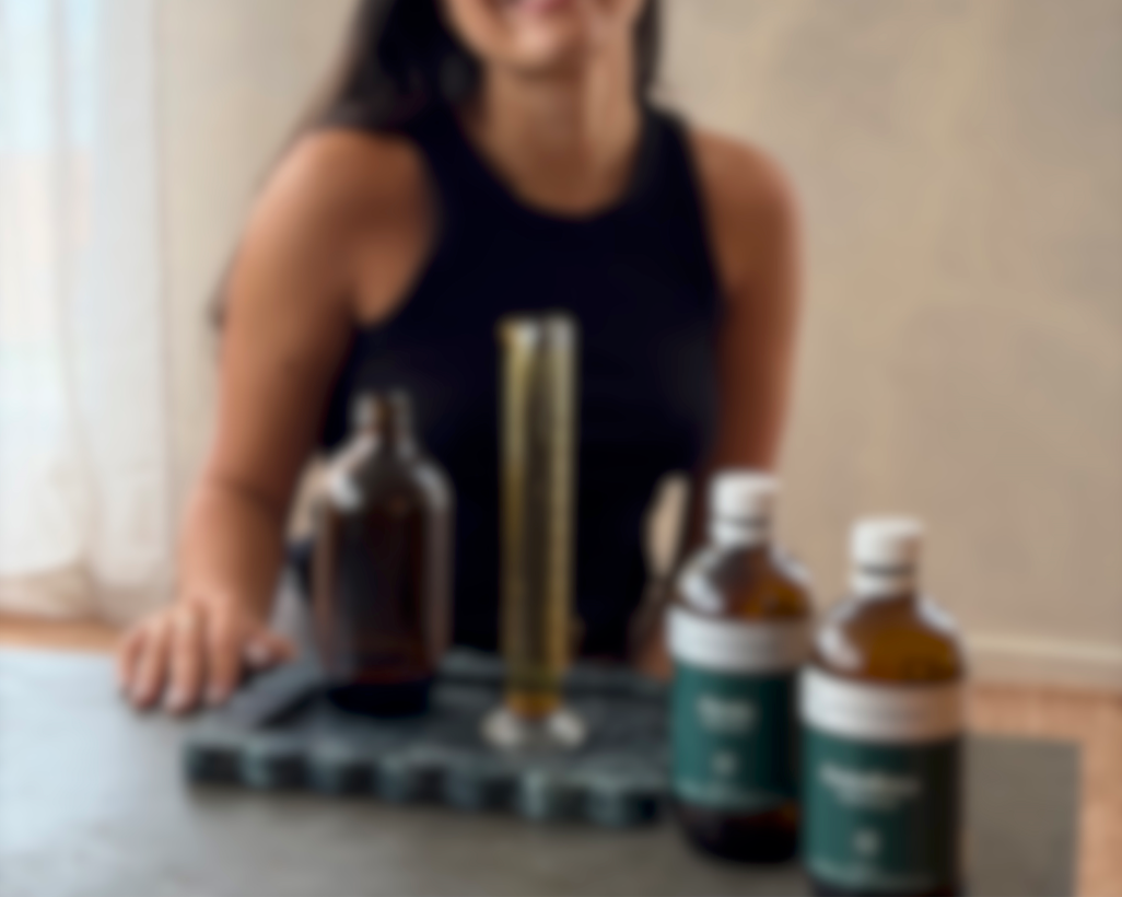 A woman sitting at a table with mediherb herbal tincture bottles and a measuring cylinder on a tray.