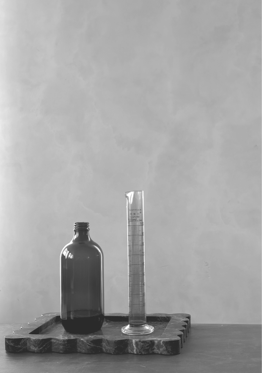 A 200ml empty amber herbal glass bottle and a graduated measuring cylinder on a wooden tray against a plain wall.