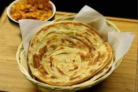 A basket with a large piece of flatbread and a small bowl of curry in the background.