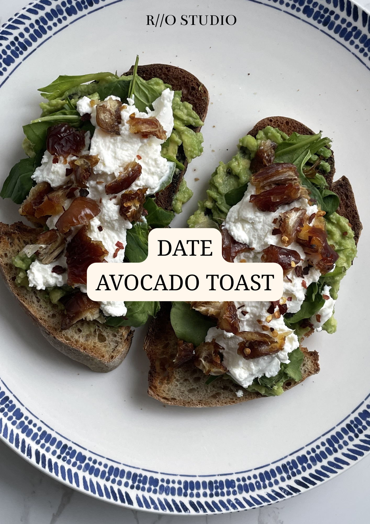 Two slices of avocado toast on a white plate with blue trim, topped with whipped cheese, avocado, sun-dried tomatoes, and greens.
