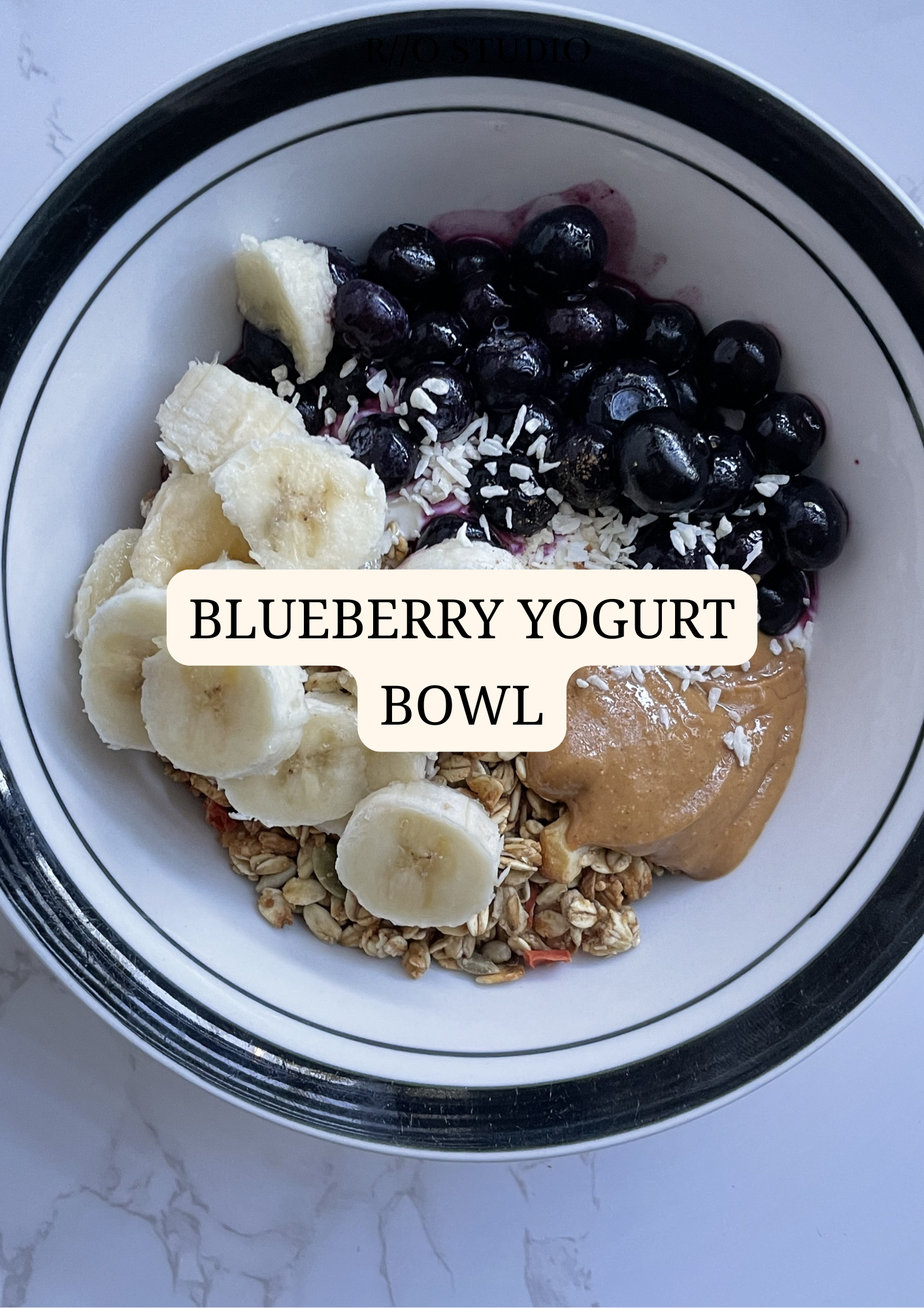 Blueberry yogurt bowl topped with shredded coconut, peanut butter and banana slices with granola