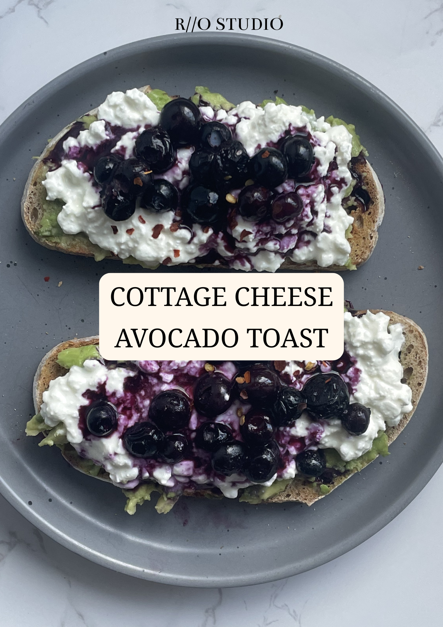 Two open-faced avocado toast slices topped with cottage cheese and blueberries on a gray plate.