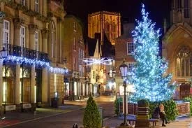 A decorated Christmas tree with thousands of lights in St Helen's Square in York city centre at night, surrounded by festive holiday lights and buildings.