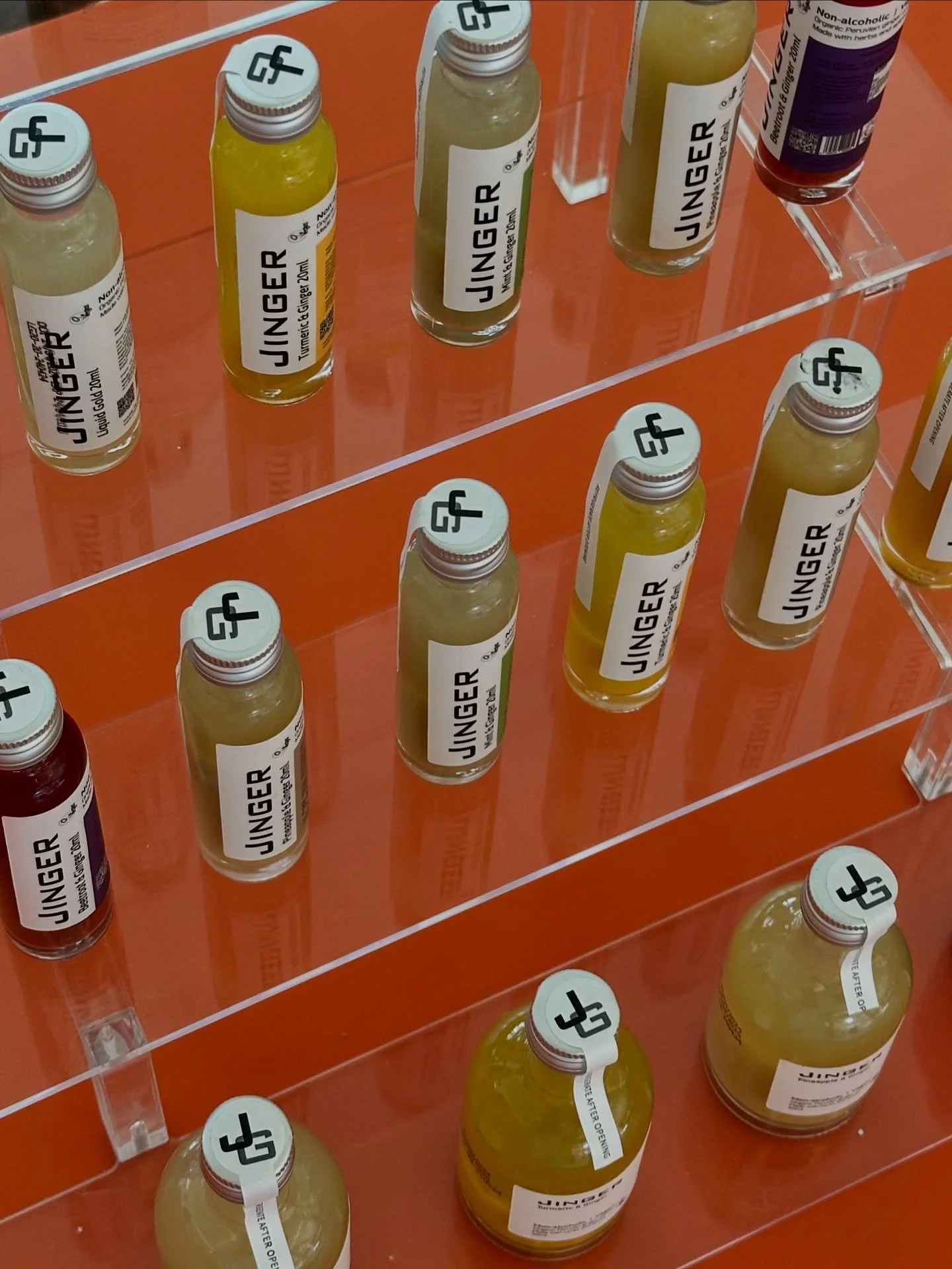 Display of small glass bottles labeled 'Ginger' with yellow liquid, arranged on transparent shelves.