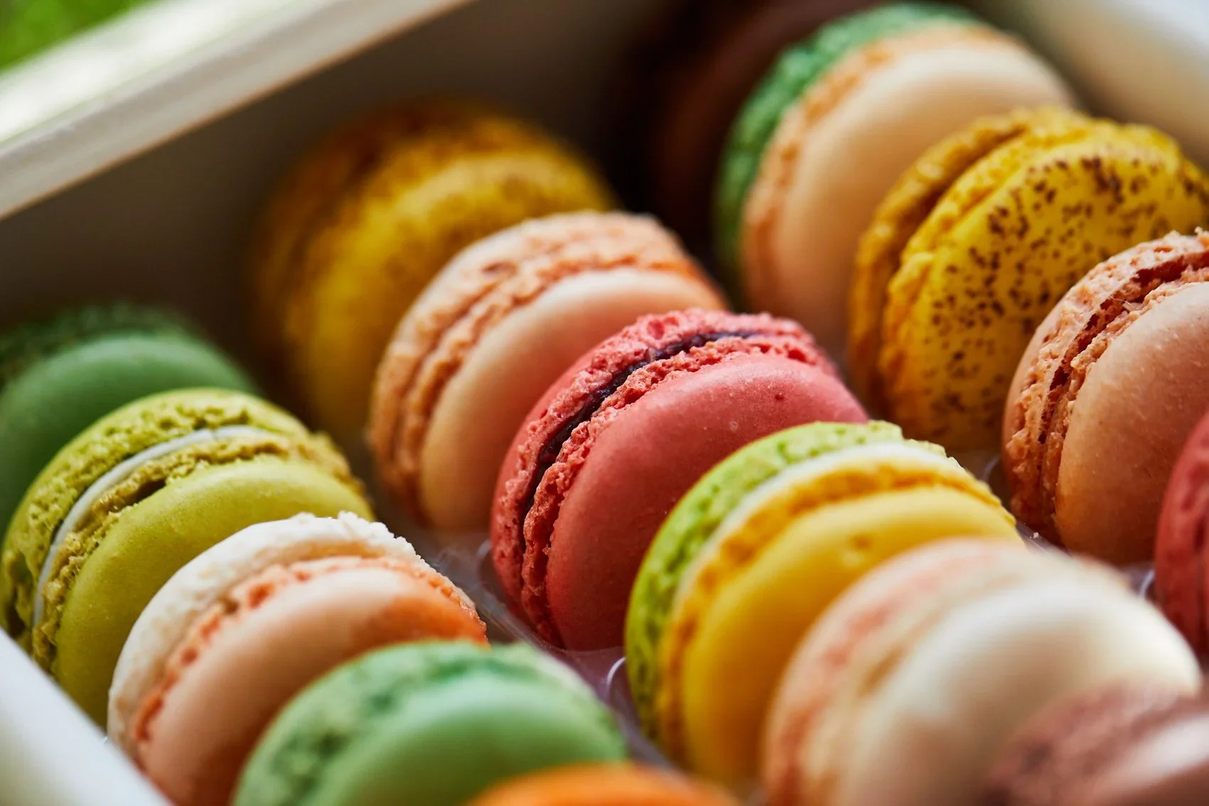 Colorful assortment of macarons in a box, featuring pink, green, yellow, orange, and beige flavors.