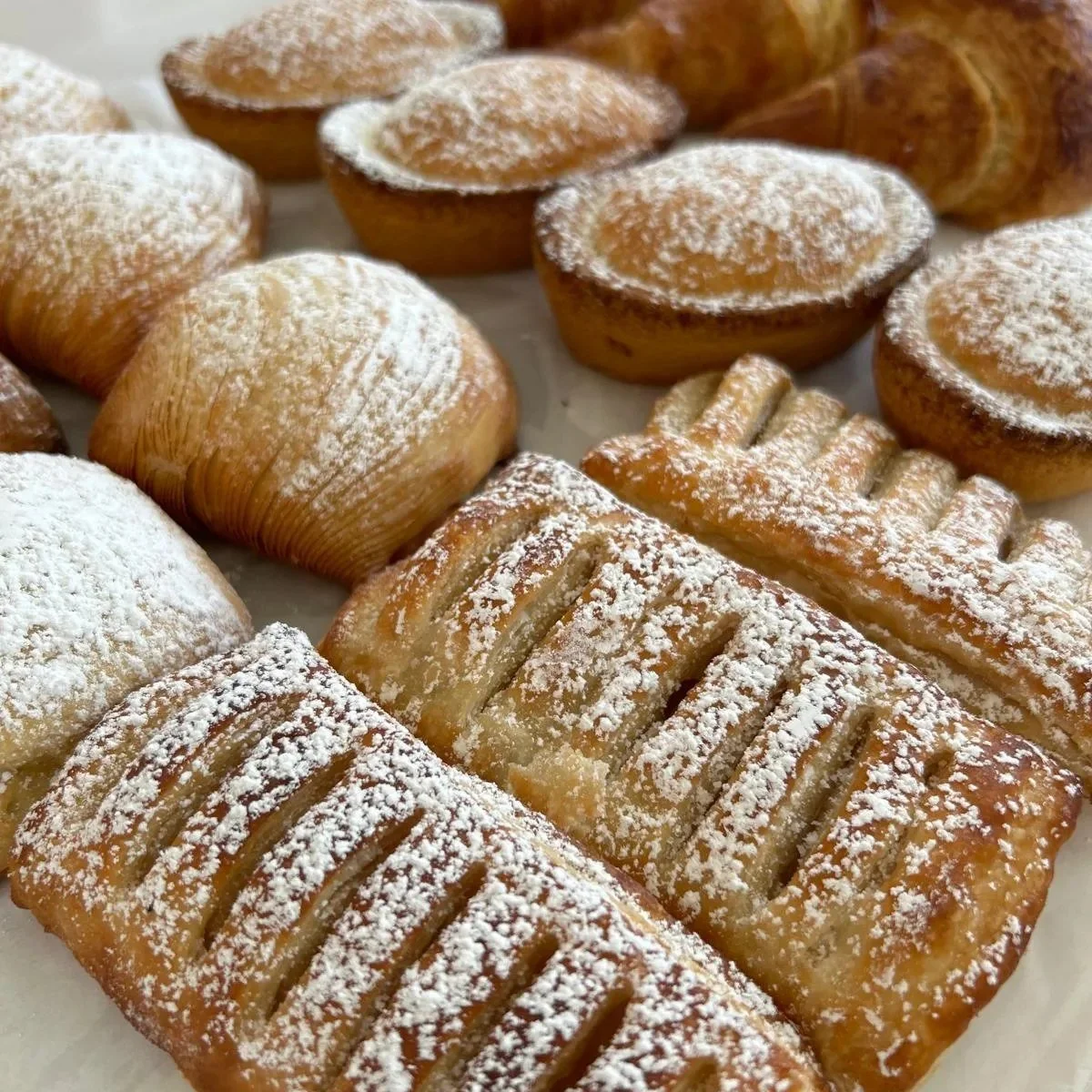 Assorted baked goods, including small round muffins and rectangular pastries dusted with powdered sugar.