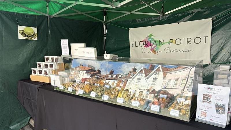 A market stall with a diorama of baked goods and signs, located under a green canopy, for Florian Poirot, a baker and pastry chef.