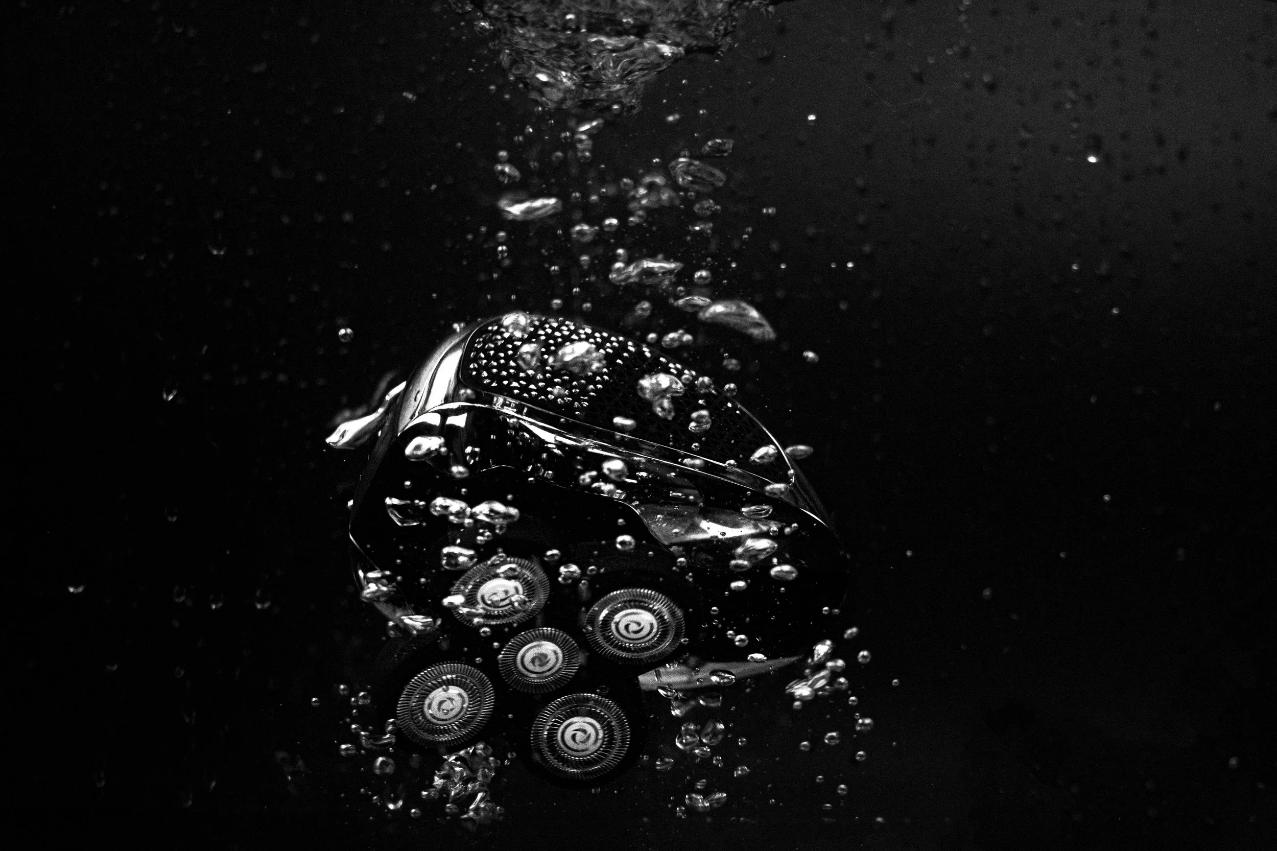 A close-up of a shaver with water droplets on its surface, submerged in water with bubbles surrounding it.
