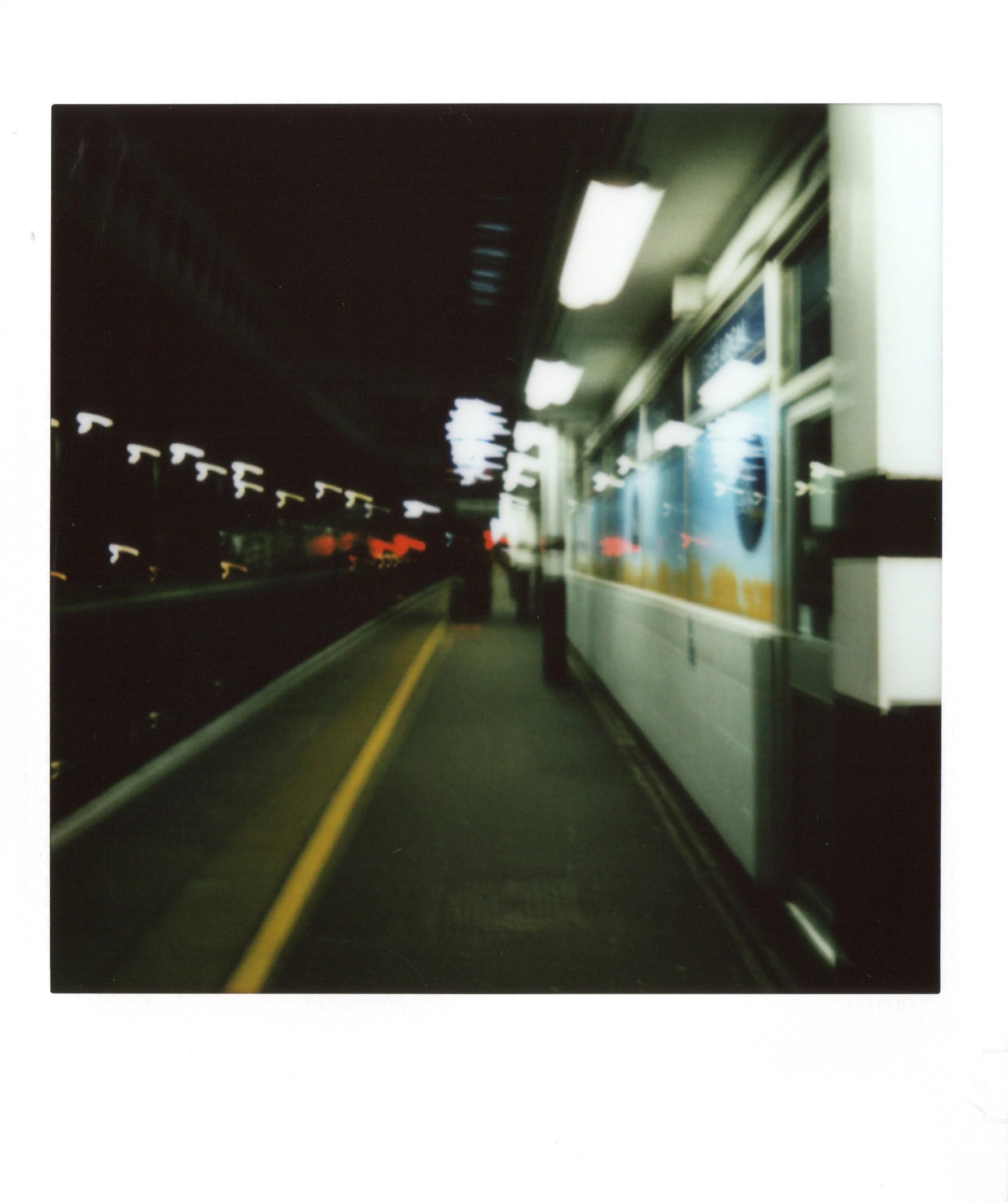 A blurry photo of a subway or train station platform at night with bright overhead lights and a few people waiting.