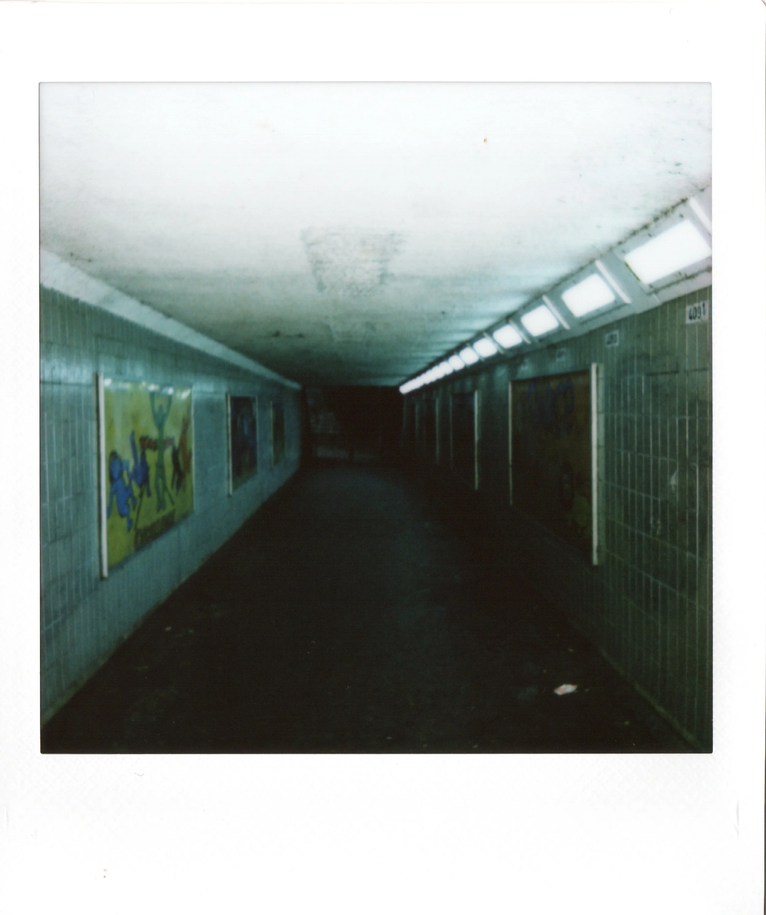 Empty underground pedestrian tunnel with tiled walls, graffiti, and fluorescent lights, leading into darkness.