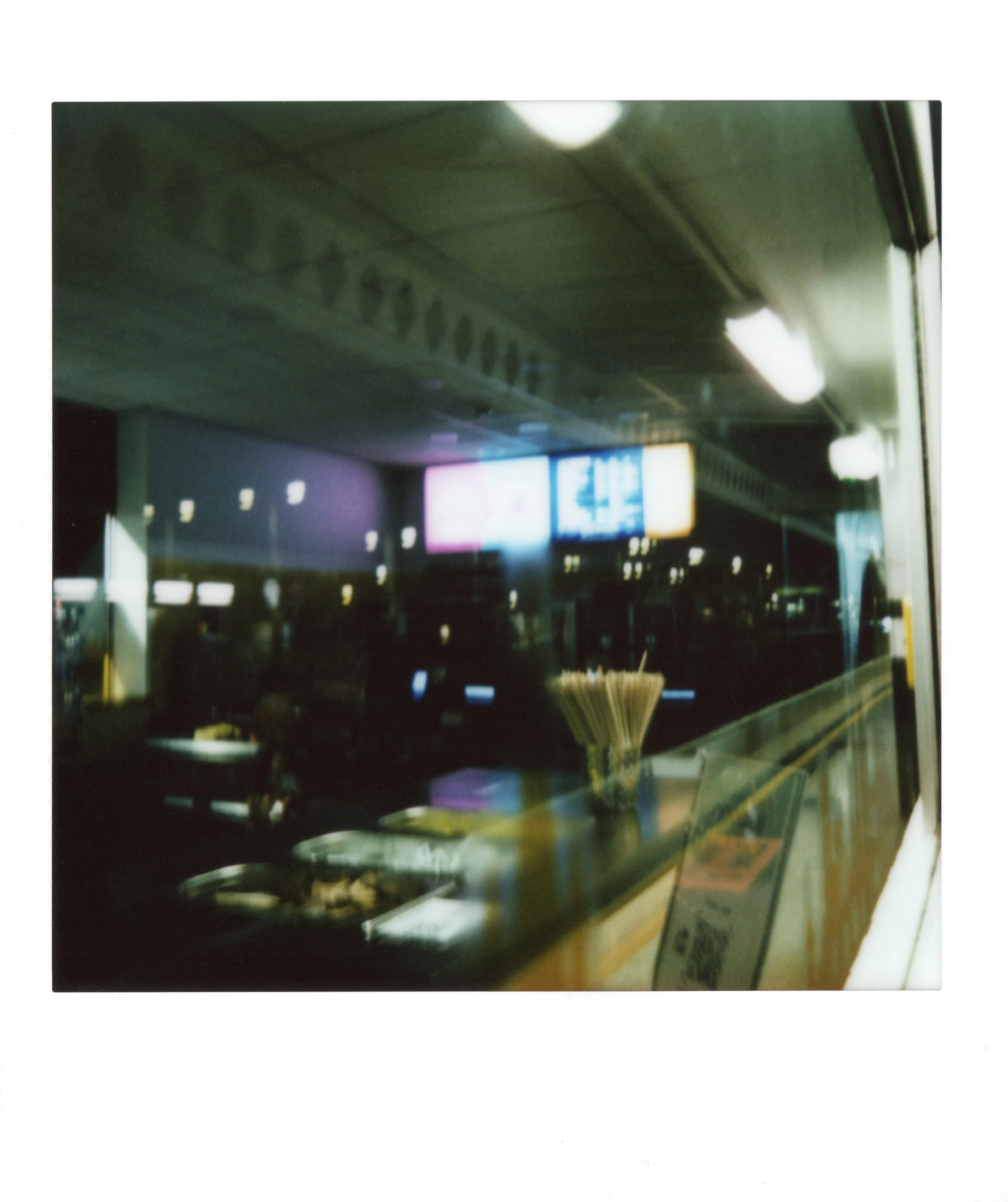 Blurred view of a city street scene at night, seen through a window, with illuminated signs and lamp reflections.