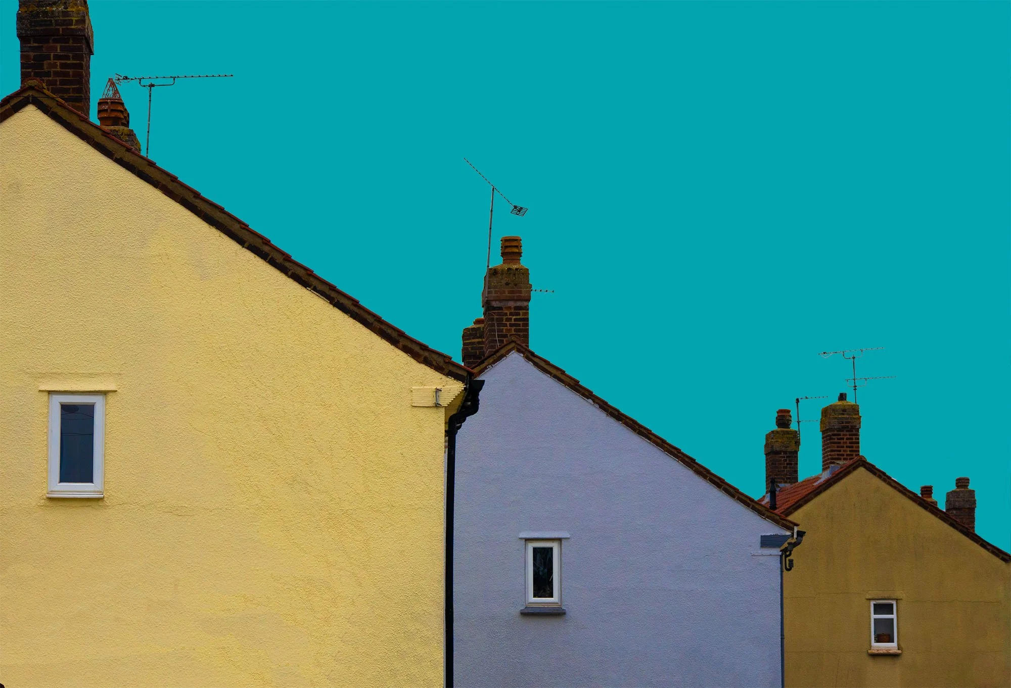 Multiple houses with yellow and gray facades and brick chimneys against a bright blue sky.