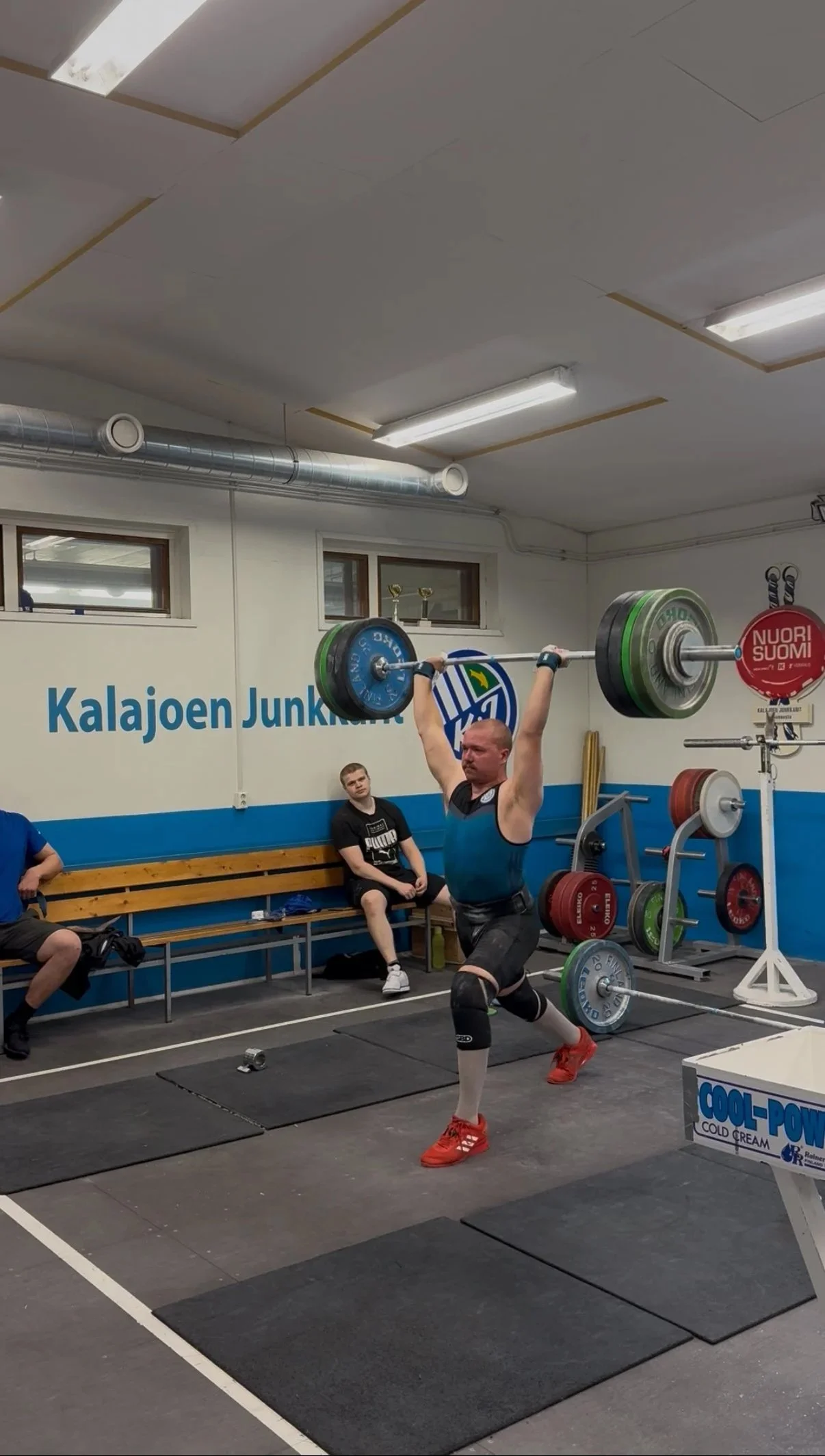 Mies tekemässä painonnostoliikettä, jossa tanko on pään yläpuolella käsien varassa.