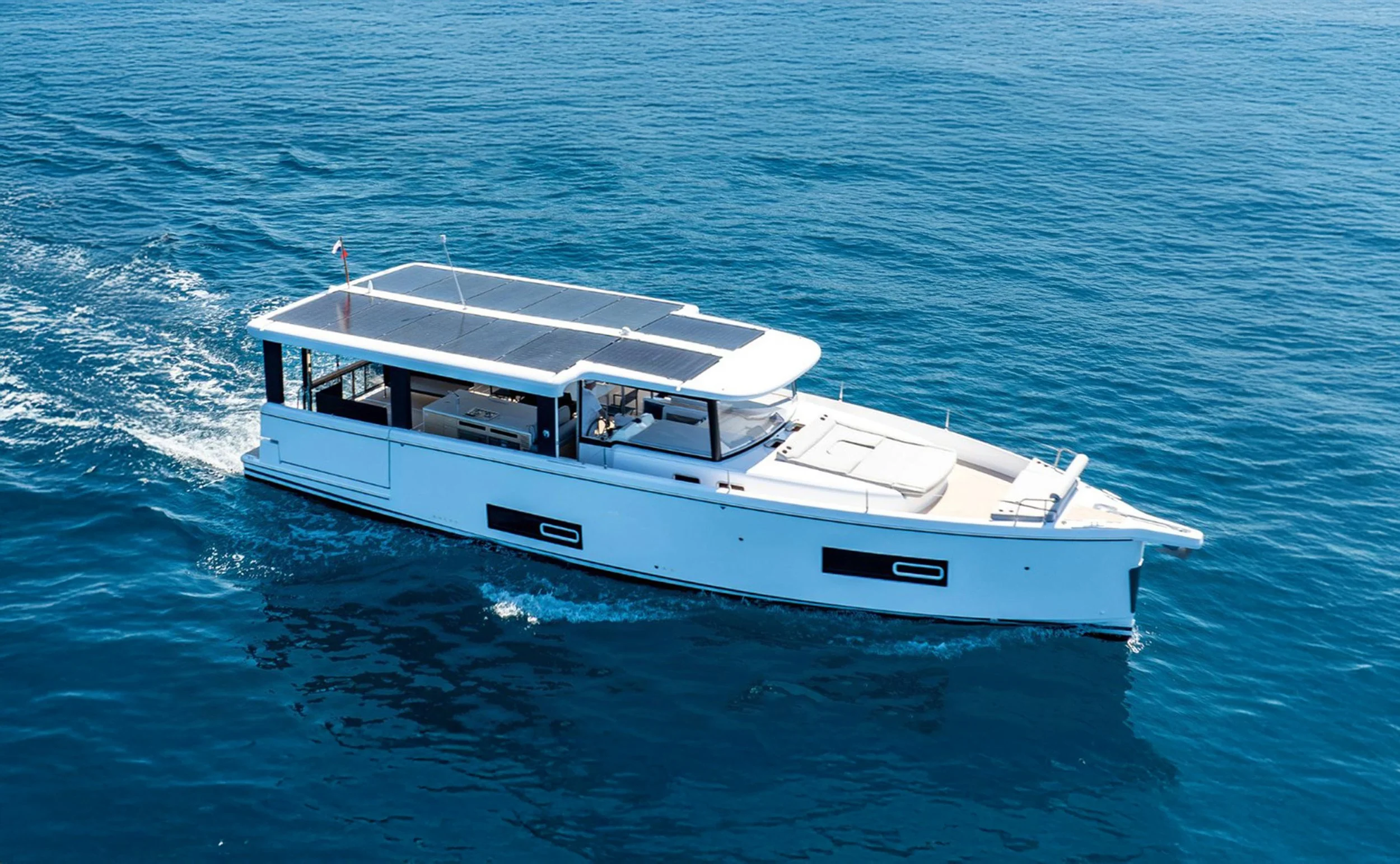 A white motor yacht with solar panels on the roof, sailing on blue ocean water.