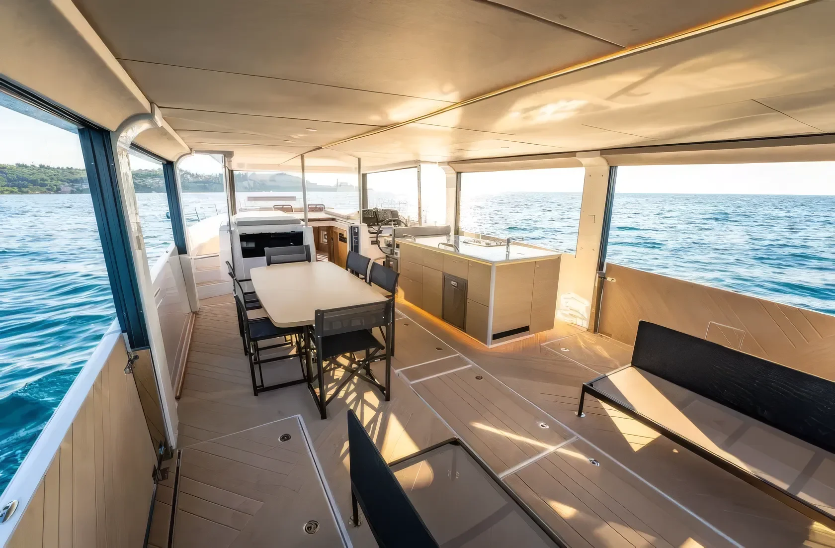Open deck of a yacht with a dining table and chairs, kitchenette, and seating area, with ocean view in the background.