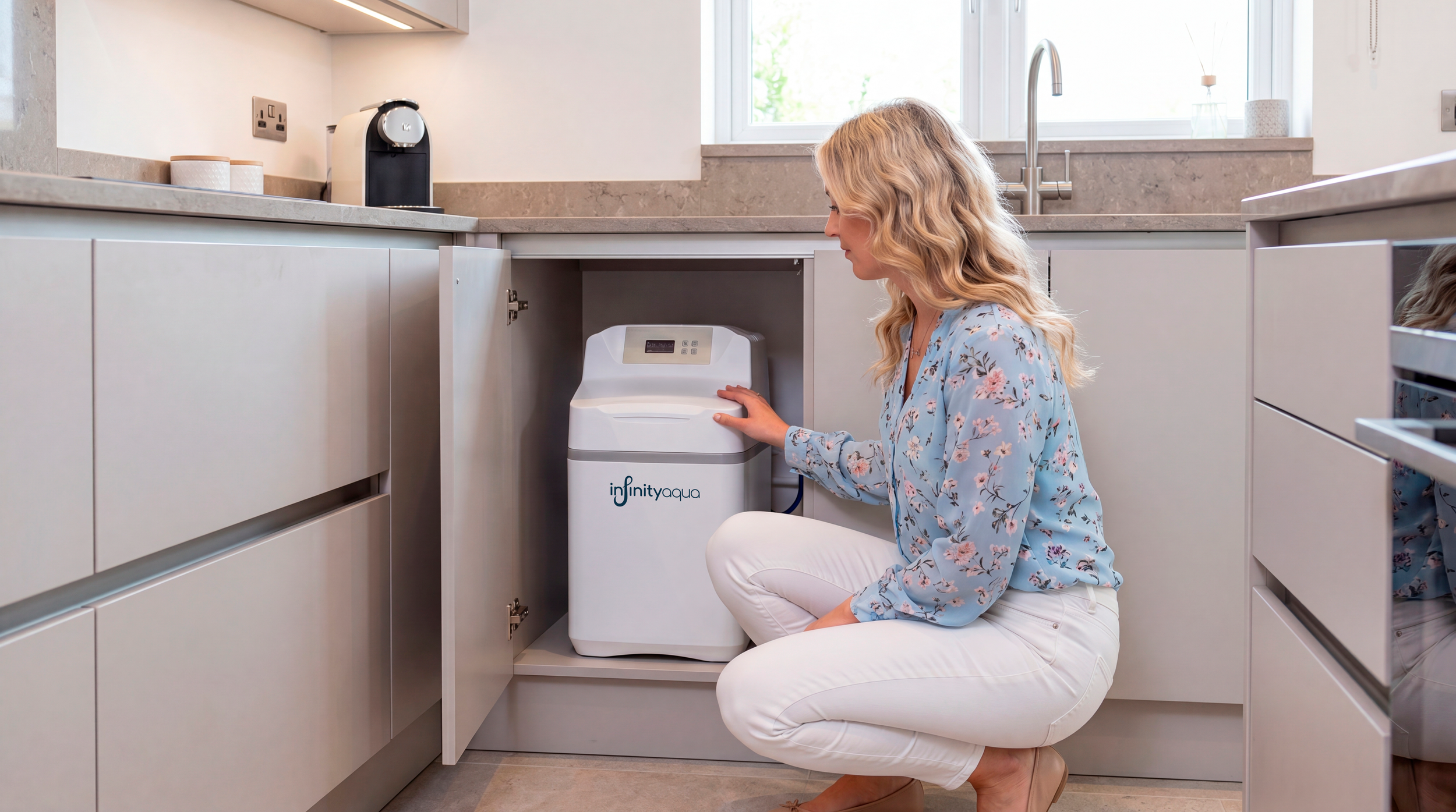 Mujer en rodillas en la cocina ajustando una lavadora portátil Infinity Aqua debajo de la encimera.