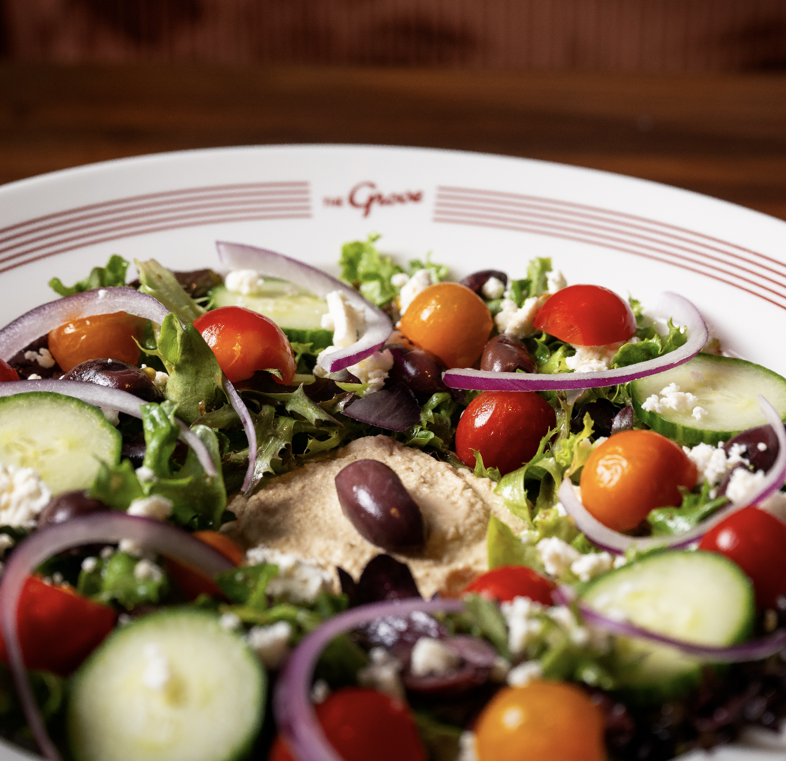 Close-up of a fresh garden salad with cherry tomatoes, cucumber slices, red onion, black beans, and crumbled cheese on a white plate with red stripes.