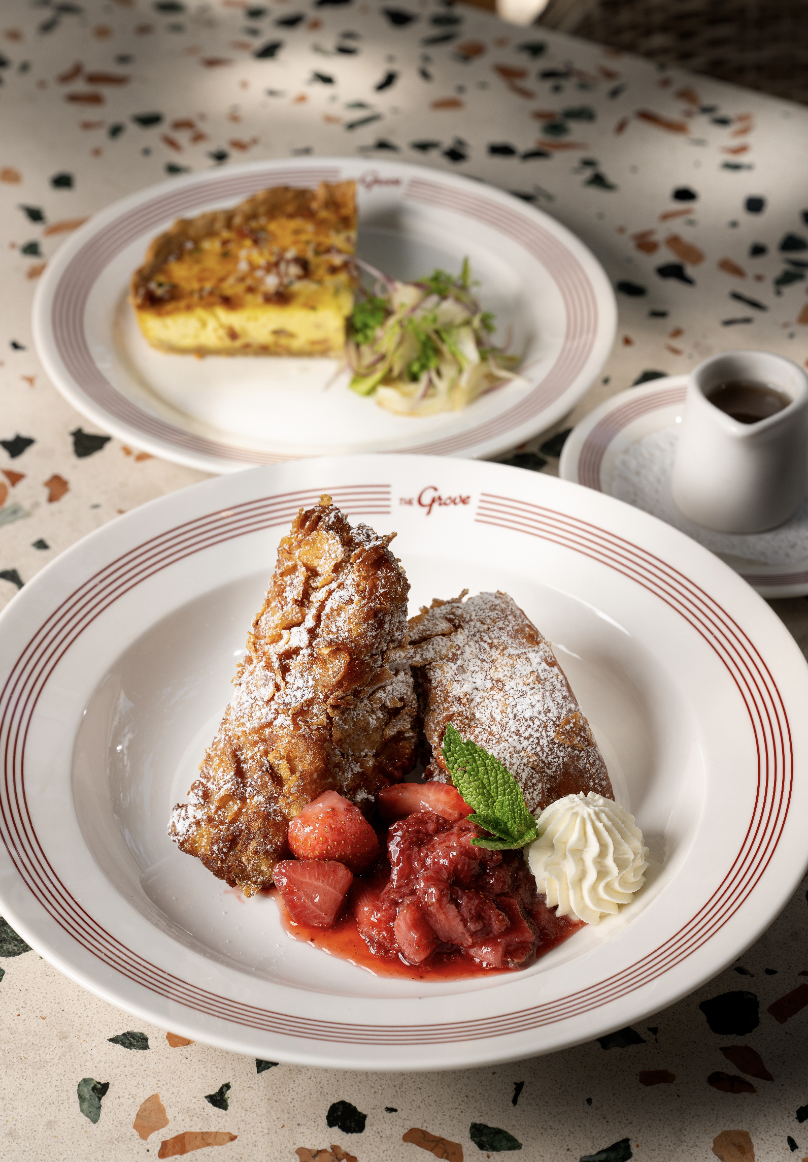 Brunch on the patio with French toast with powdered sugar, fresh strawberries, strawberry compote, whipped cream, and a mint leaf on a white plate with red stripes.