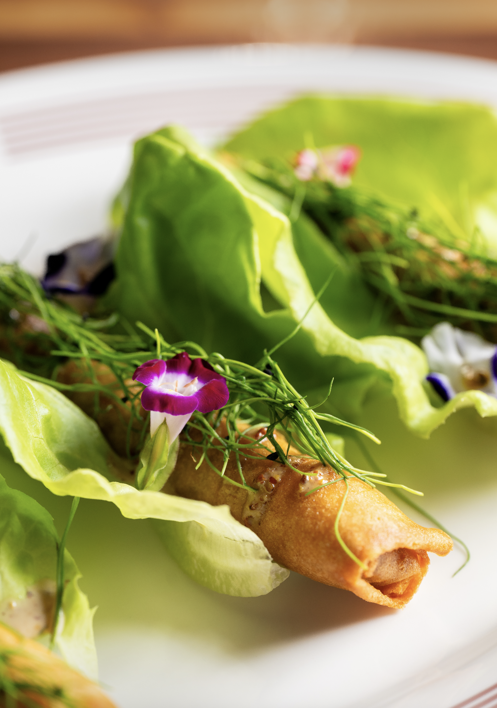 Cubano spring roll garnished with edible flowers and herbs on a white plate. Inspired by the Cuban sandwich.