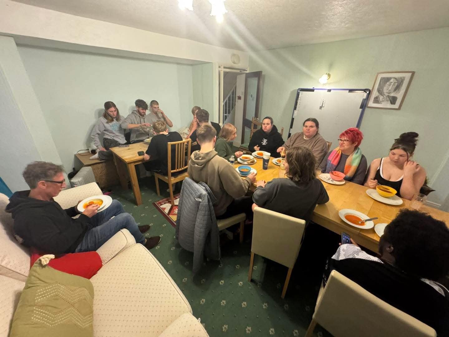 Group of people gathered around a dining table having a meal in a cozy living room.