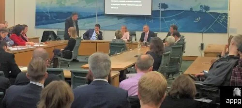 NADSN | National Association of Disabled Staff Networks | An Wide Shot From the Back of a Conference Room Shows a Group of People Sitting Around a Large U-Shaped Wooden Table