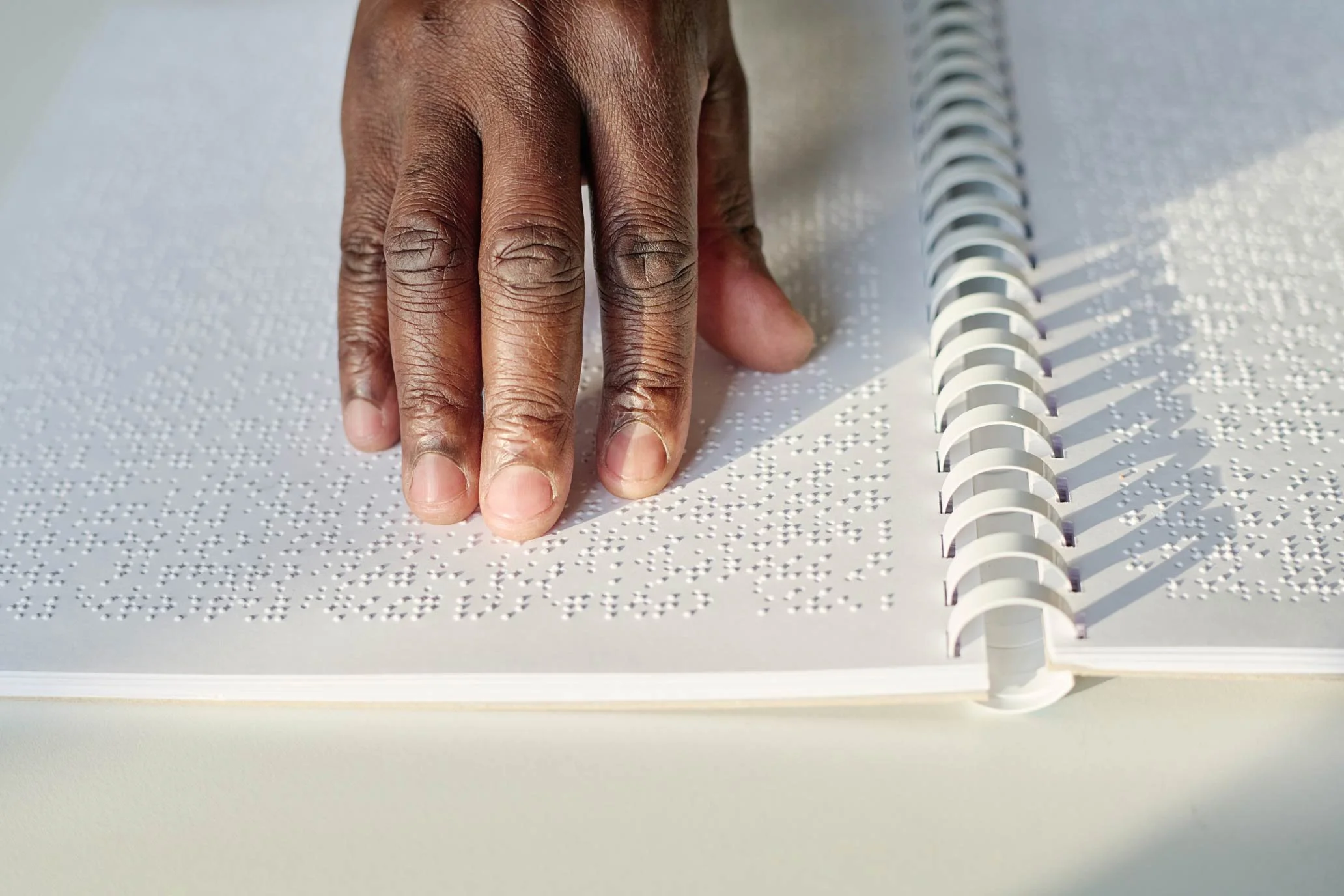 NADSN | National Association of Disabled Staff Networks | A Person’s Hand Resting on a Page of Braille Text in a Spiral-Bound Notebook.