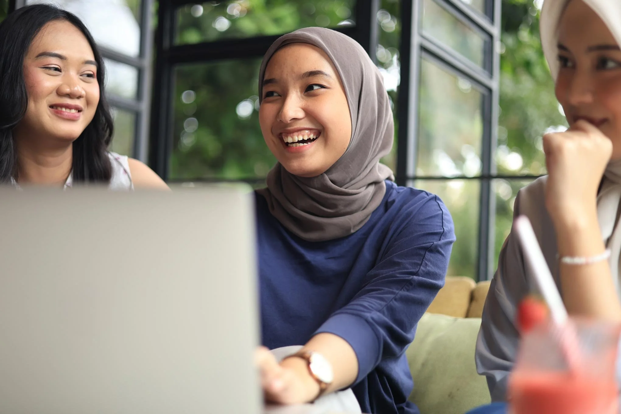 NADSN | National Association of Disabled Staff Networks | A Smiling Young Woman Wearing A Grey Hijab And A Navy Blue Top Is Working On A Laptop