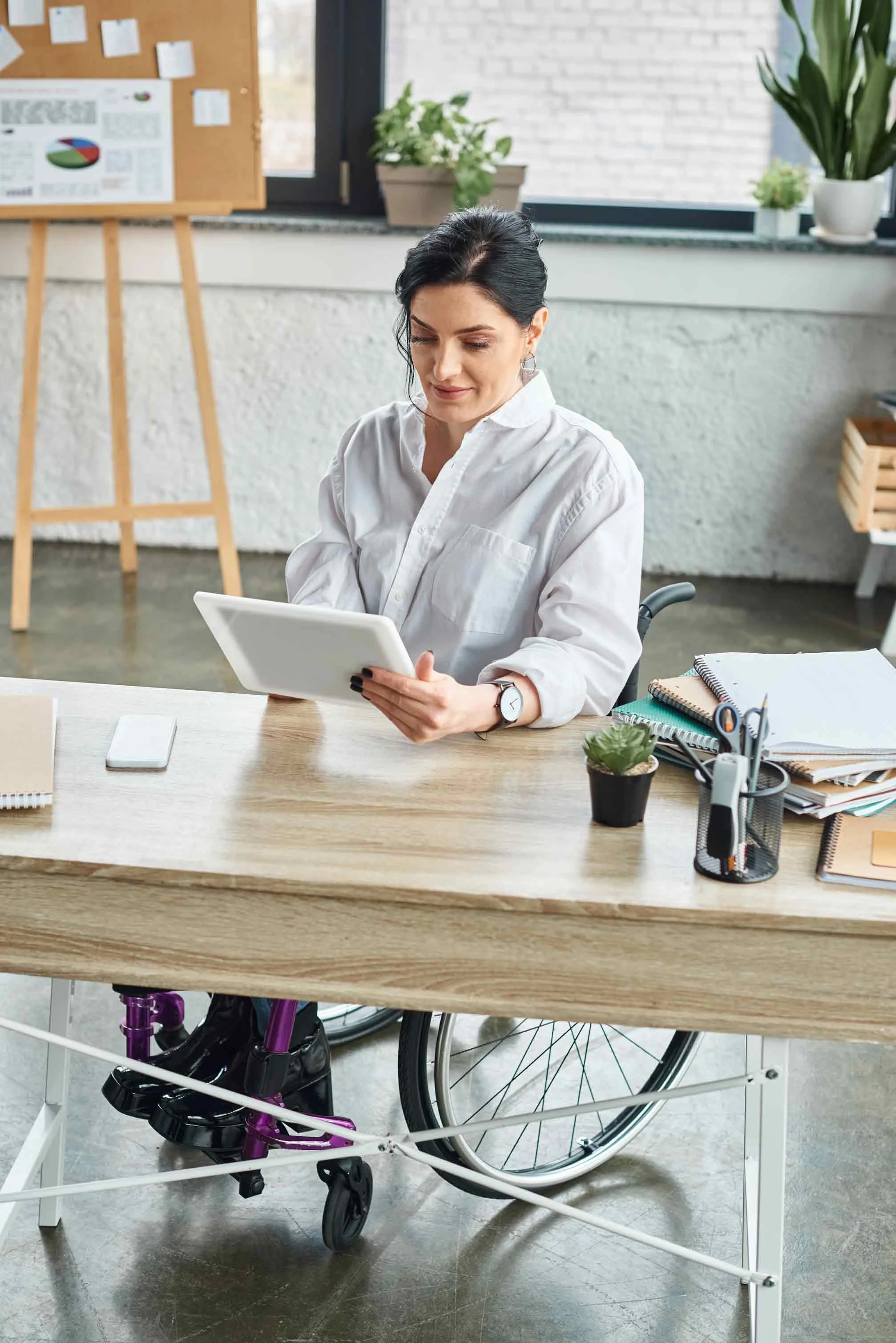 NADSN | National Association of Disabled Staff Networks | Woman in a Wheelchair Sitting at a Desk Looking at an iPad