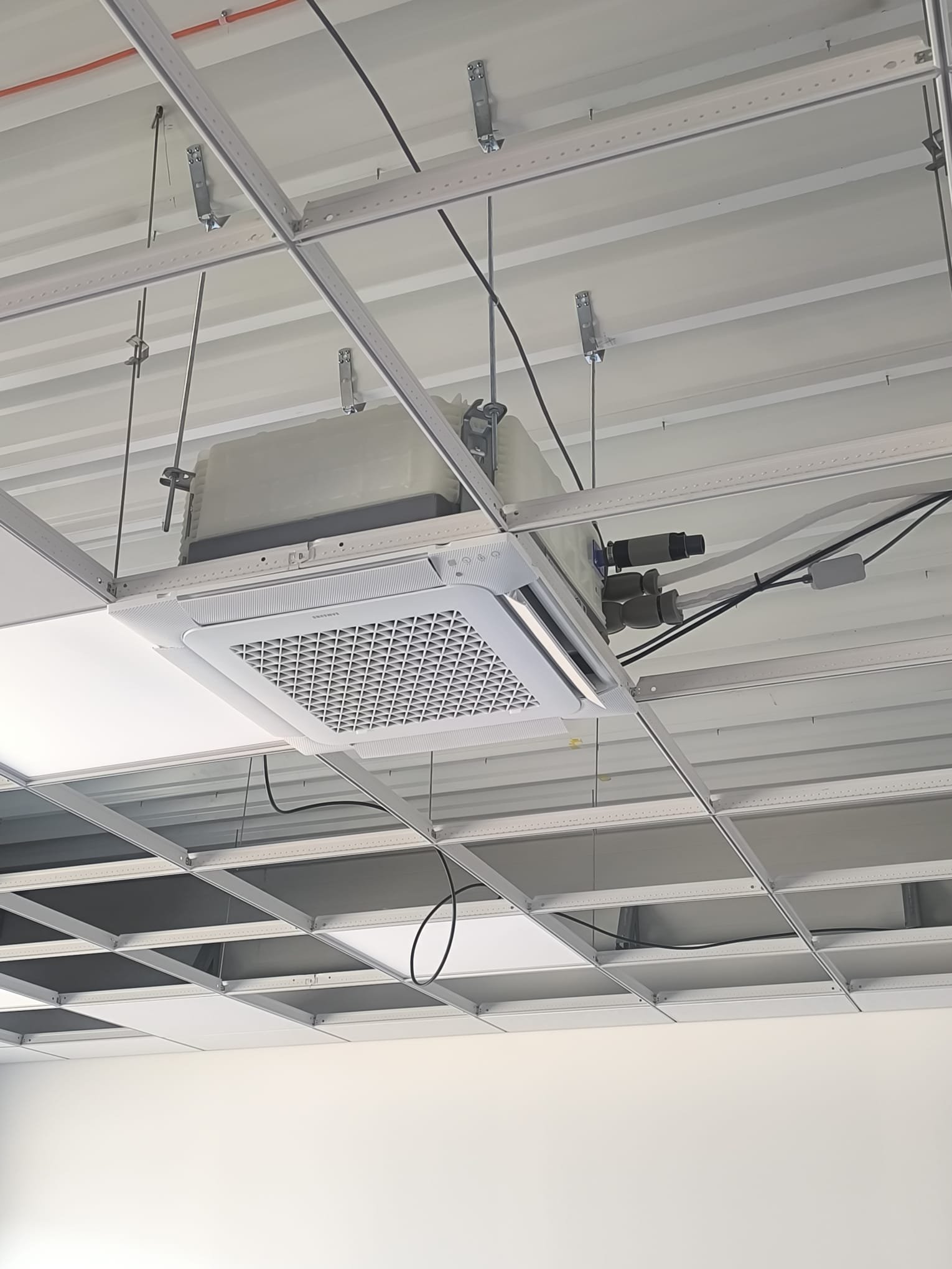 Strop s kovovou konštrukciou a zabudovanou kazetovou klimatizačnou jednotkou Samsung, spolu s ventilačnými prvkami a elektrickým vedením, vhodný pre komerčné priestory a moderné HVAC inštalácie.