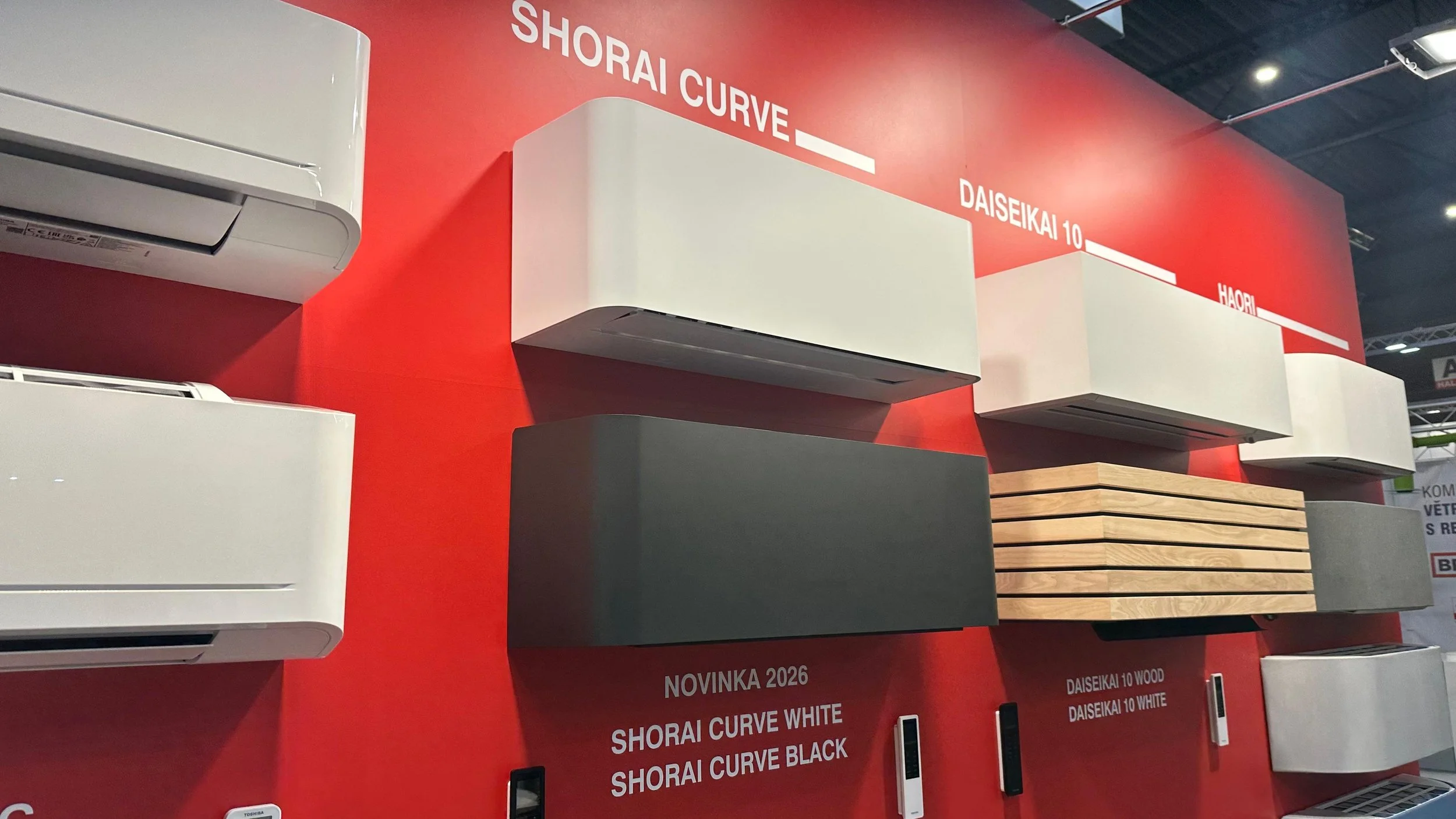 Prezentácia rôznych moderných nástenných klimatizačných jednotiek na červenom pozadí s označeniami modelov ako Shorai Curve, Daisekai a Haori, spolu s popismi produktových vlastností vrátane prevedenia v drevenom dekore a bielej farbe
