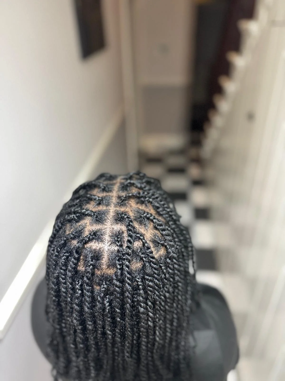 Top view of a person's head with freshly styled, thin braided hairstyle with a middle parting, in a room with a black and white checkered floor.