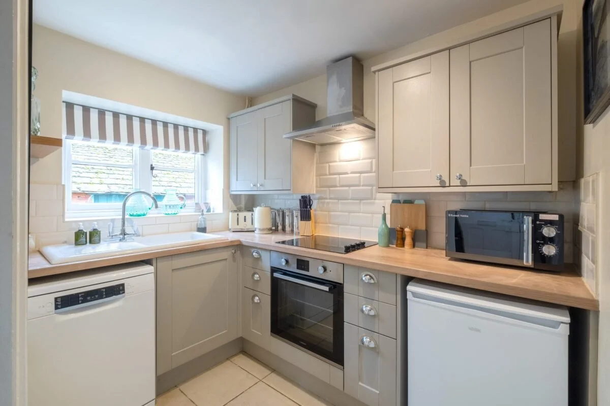 Kitchen with beige cabinets, a window with striped blinds, a backsplash with white subway tiles, black stove with oven, microwave, small freezer, dishwasher, and countertop appliances.