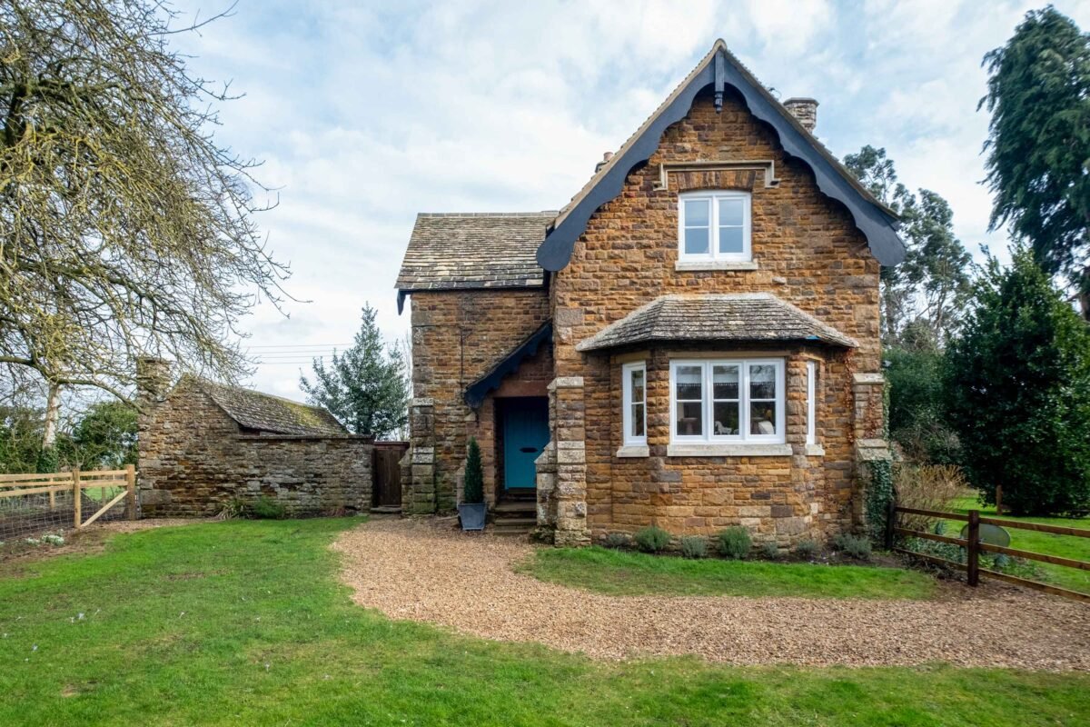 A traditional two-story cottage with a gabled roof, seasonal decor, and a small front yard with a gravel pathway.