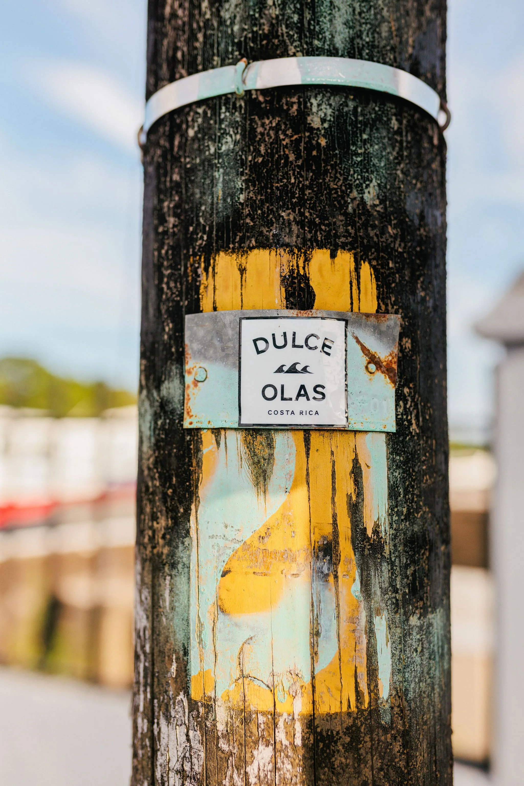 Close-up of a weathered wooden utility pole with a faded painted design and metal sign that reads "DULCE OLAS COSTA RICA" attached to it.