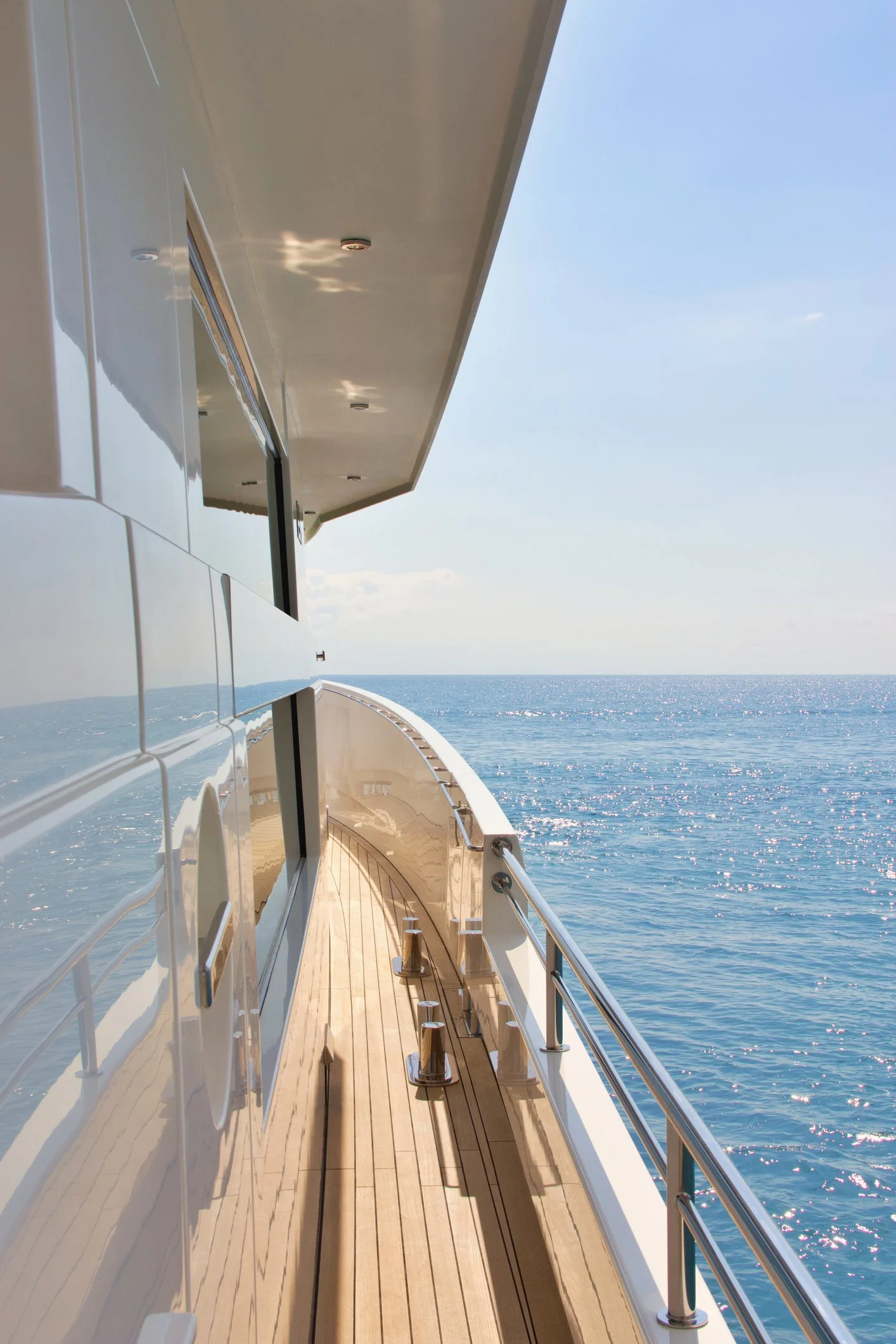 Side deck of a luxury yacht with wooden flooring, white exterior walls, and a metal railing overlooking the ocean , showcasing Over Oceans Yacht Interiors Projects