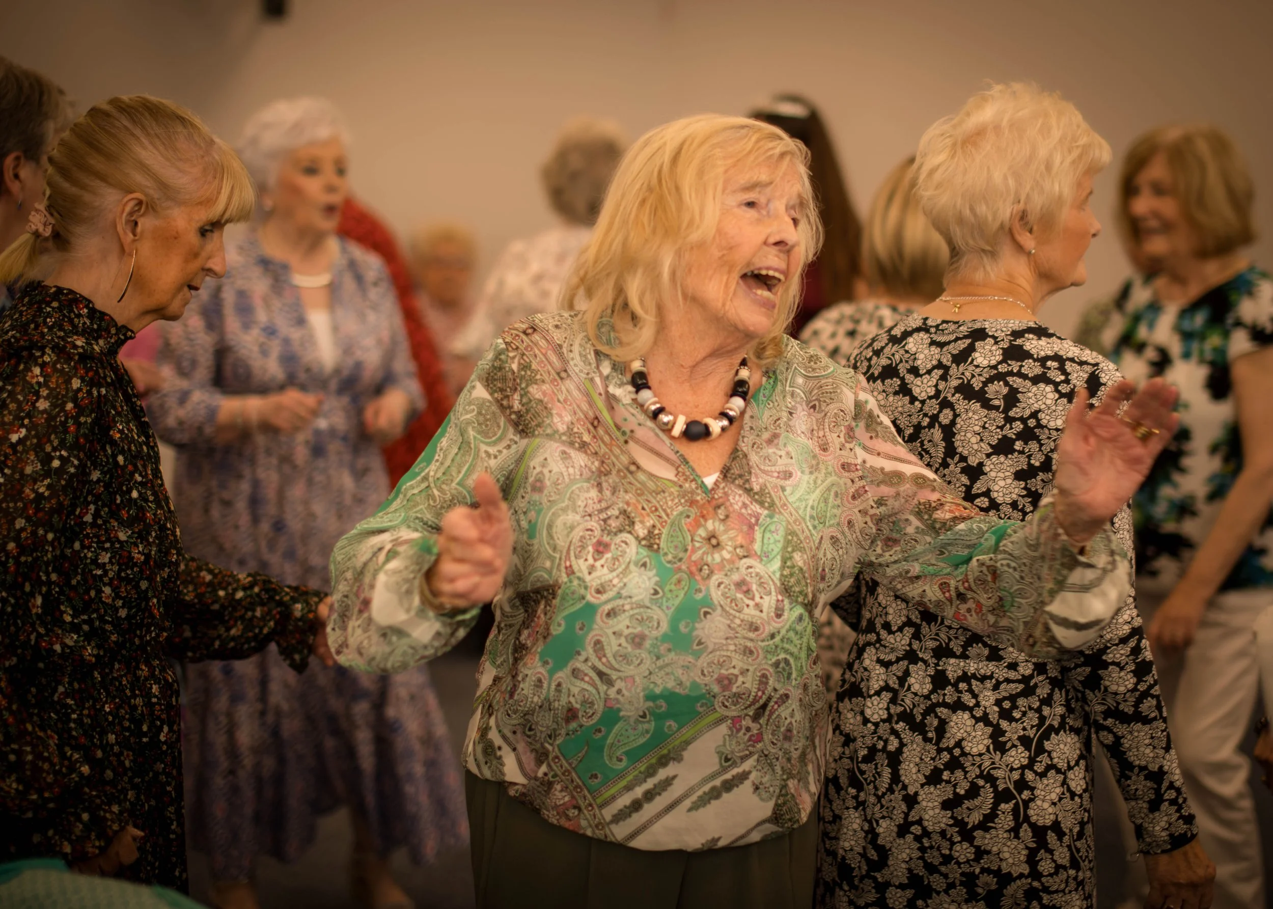 A group of senior women dancing and enjoying themselves at a social gathering in an indoor setting.