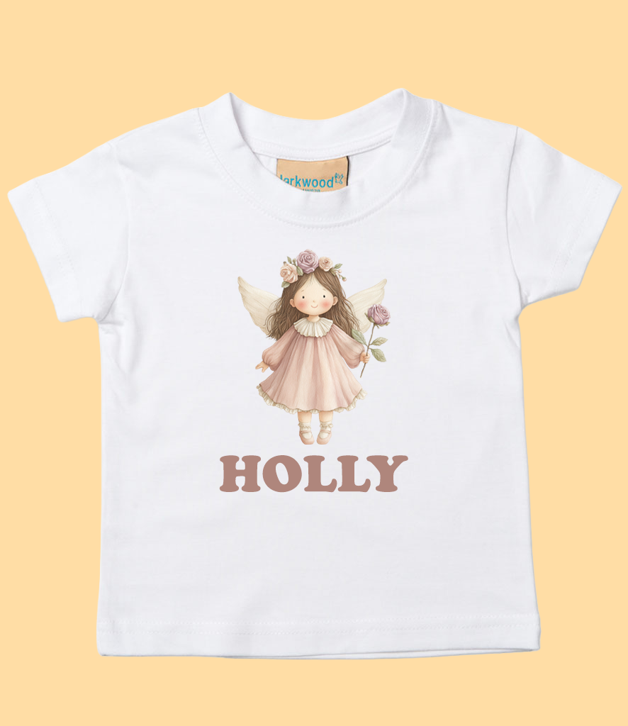 White children's T-shirt with a cartoon illustration of a fairy girl with wings, wearing a pink dress and a flower crown, holding a flower, and the name 'Holly' printed below.