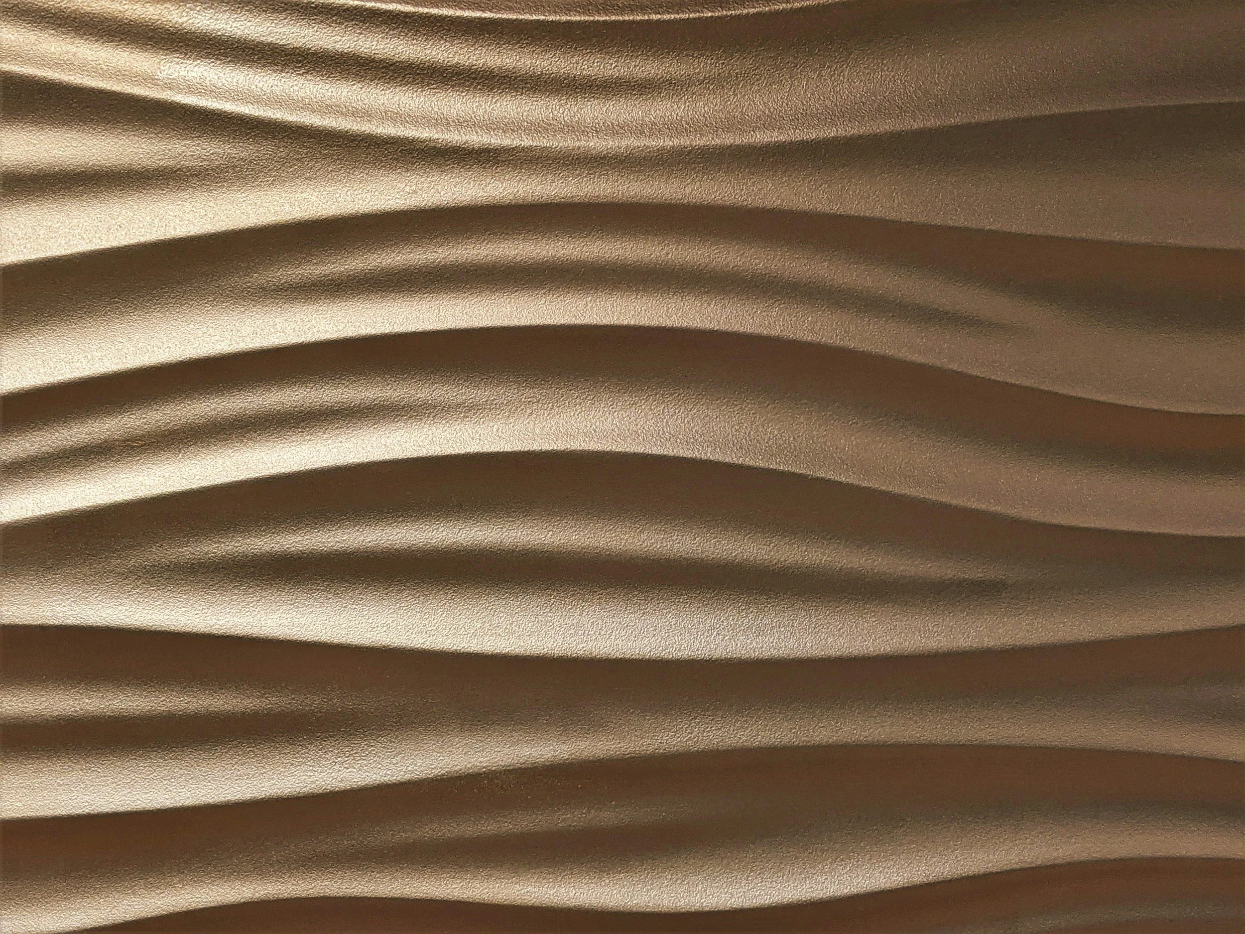 Close-up image of a textured, wavy metallic surface with a gold or brass finish.