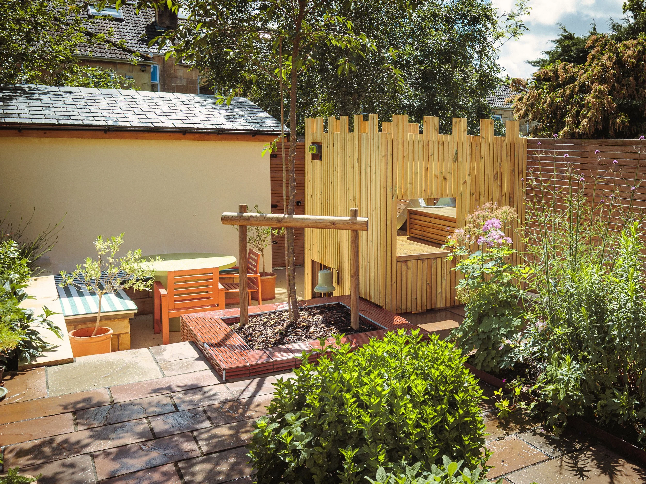 Tiled planter shining in the sun after a quick downpour. Herb bed and perennial bed in the forefront