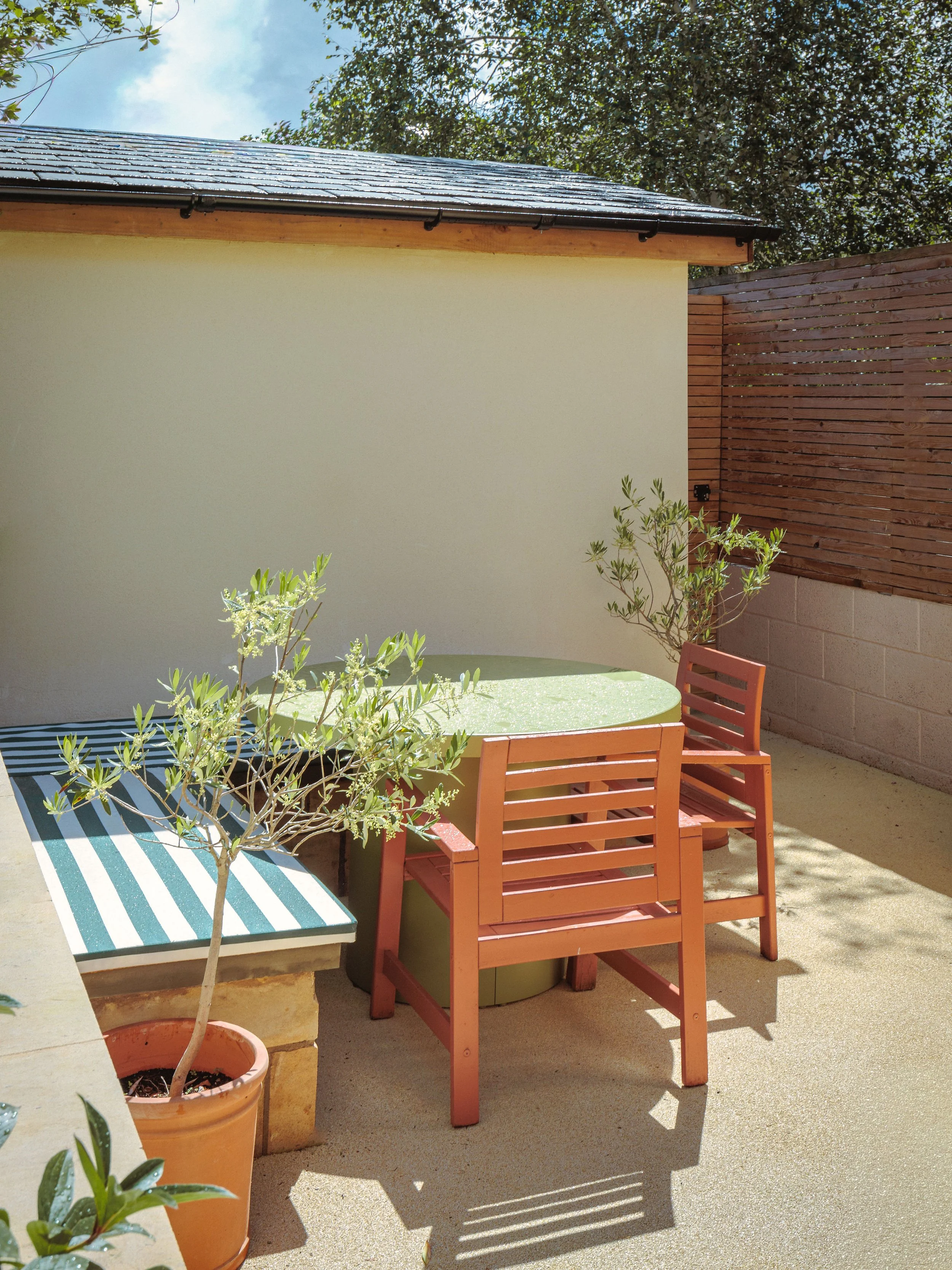 Outdoor dining area framed by two potted olive trees and a newly built & rendered shed
