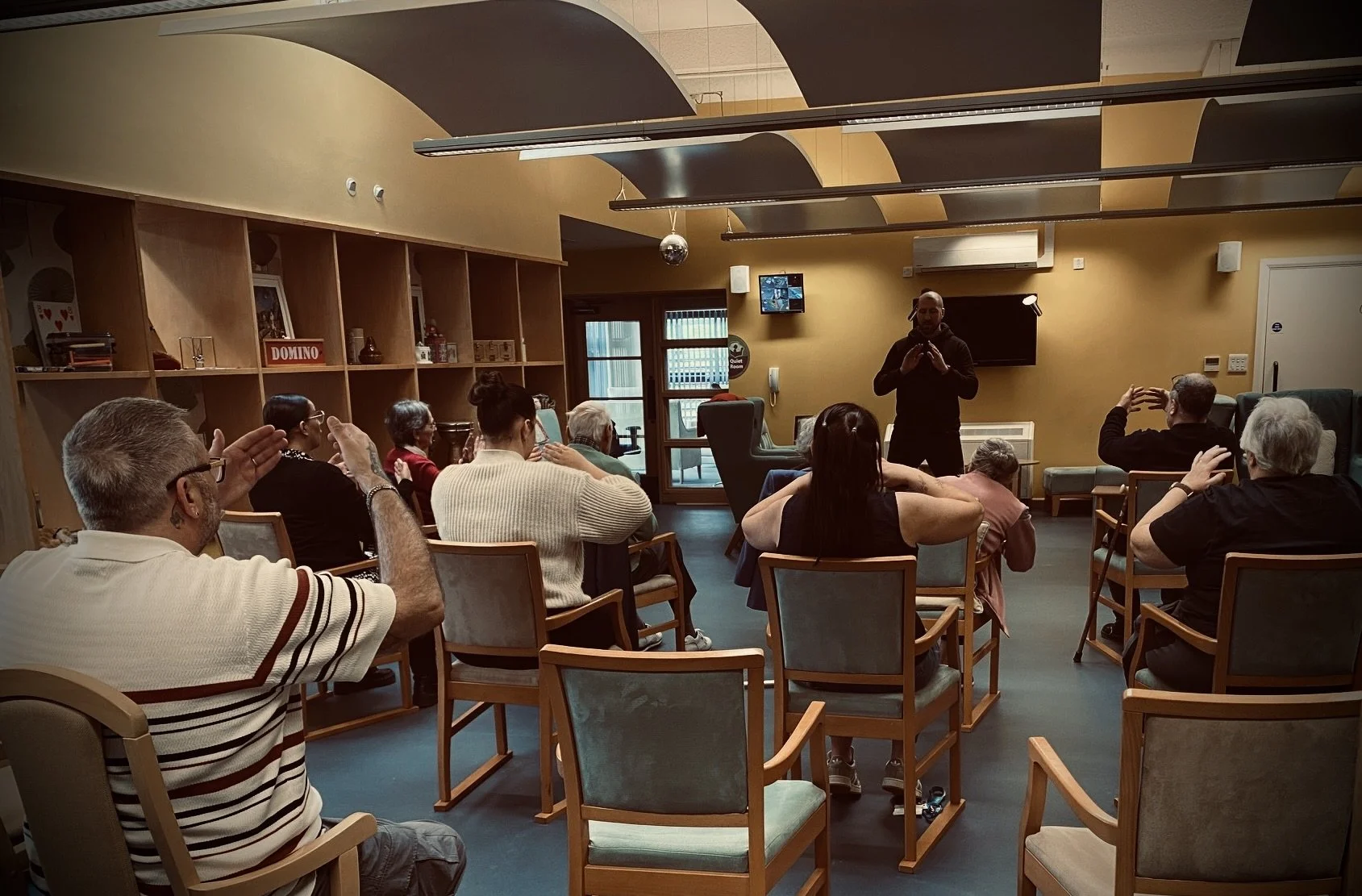 A community group follow a Qigong workshop in a cozy indoor space.
