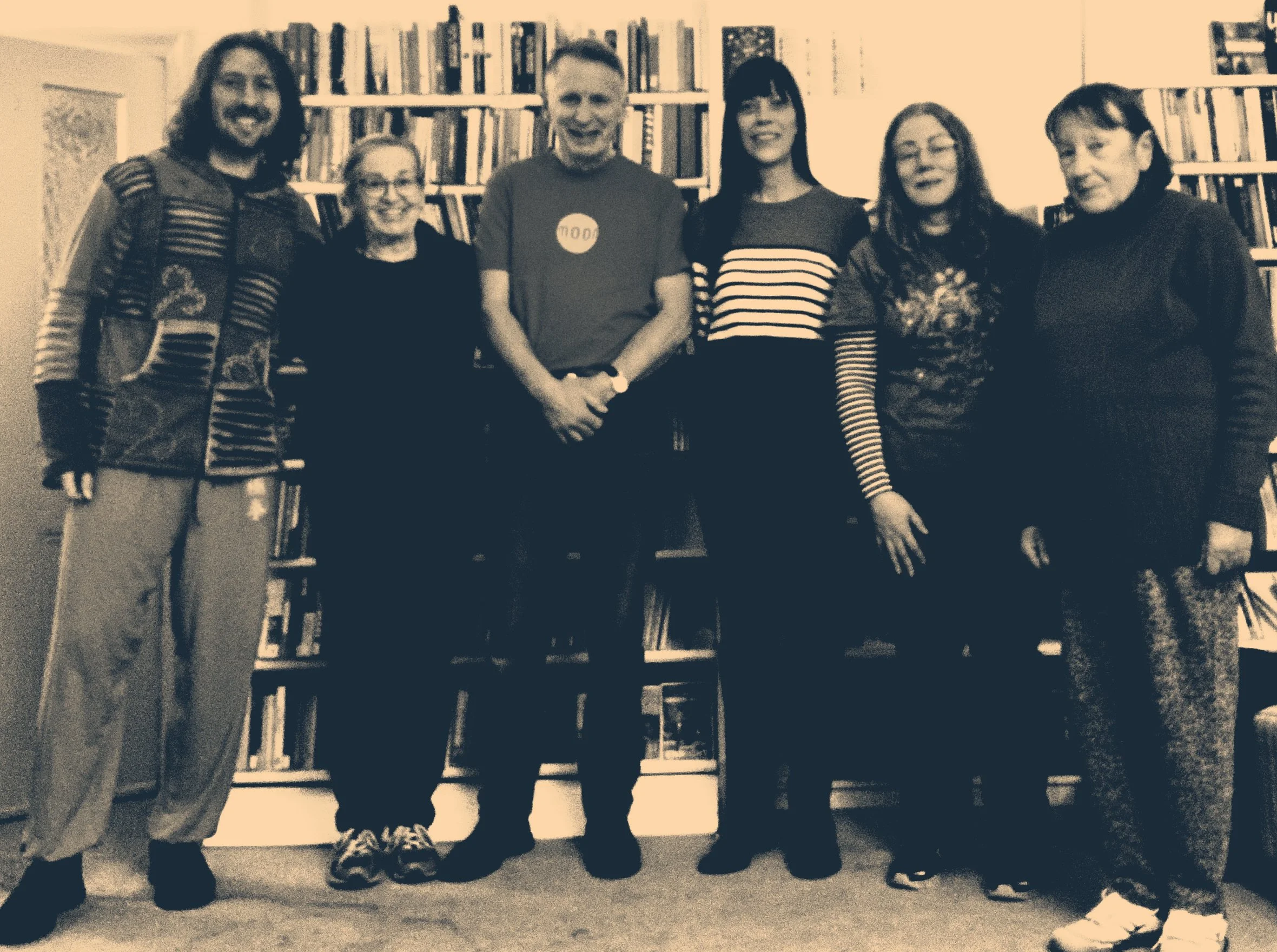 Group of six Qigong participants standing in front of a bookshelf in a library or bookstore, smiling at the camera.