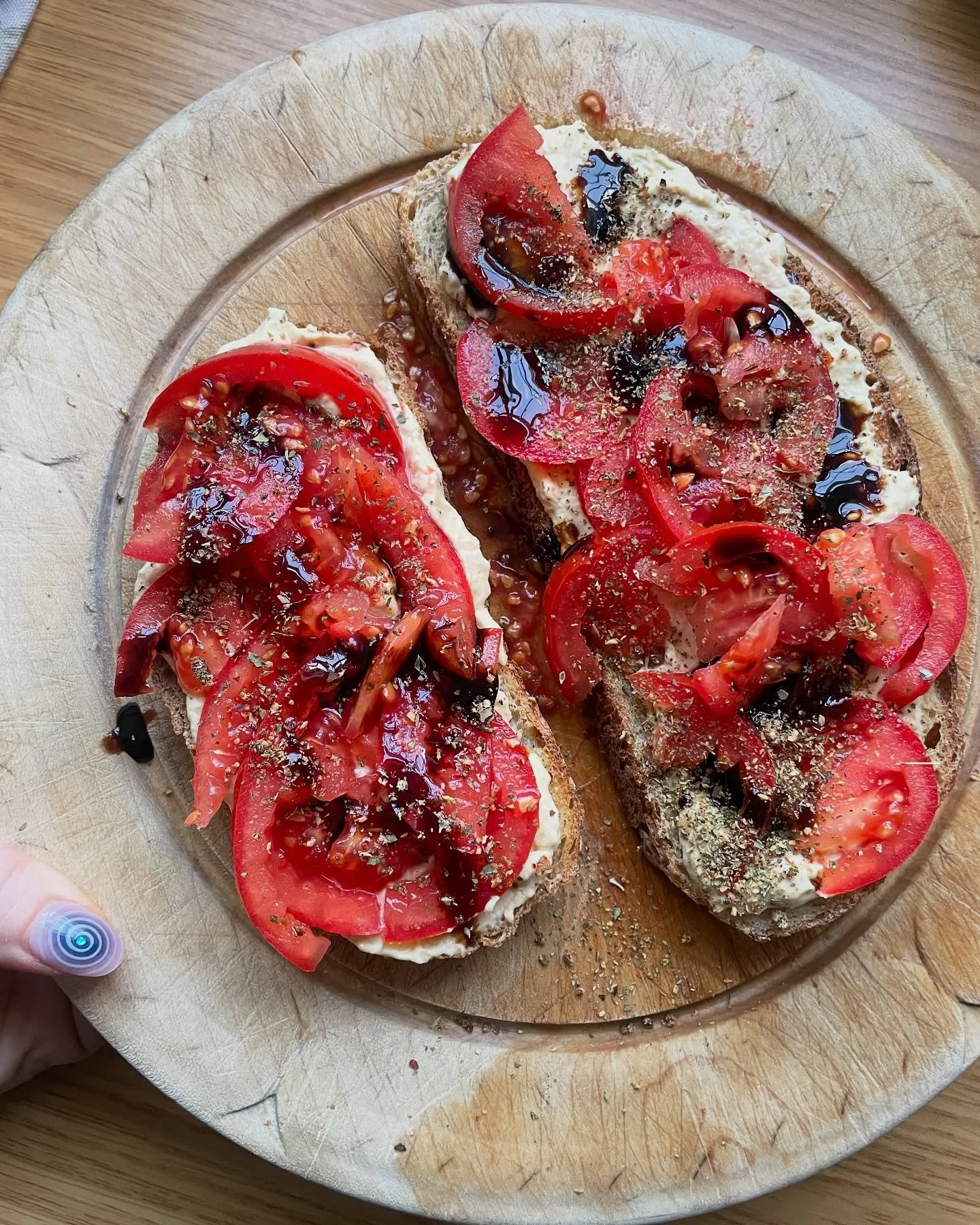 Sliced baguette bread topped with tomato slices, cream cheese, balsamic glaze, and herbs on a wooden cutting board.