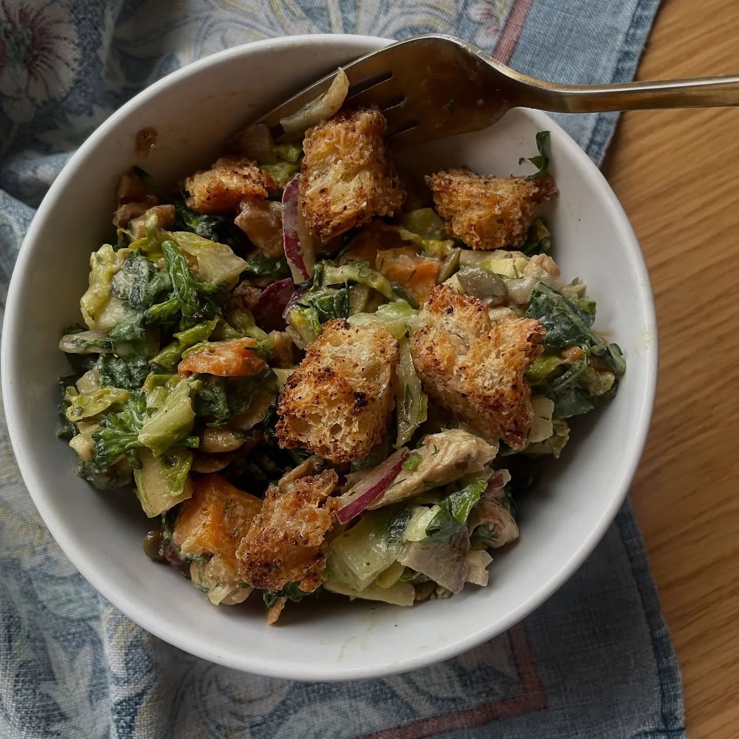 Bowl of vegetarian salad with mixed greens, chopped vegetables, and croutons on top, served with a fork on the side.