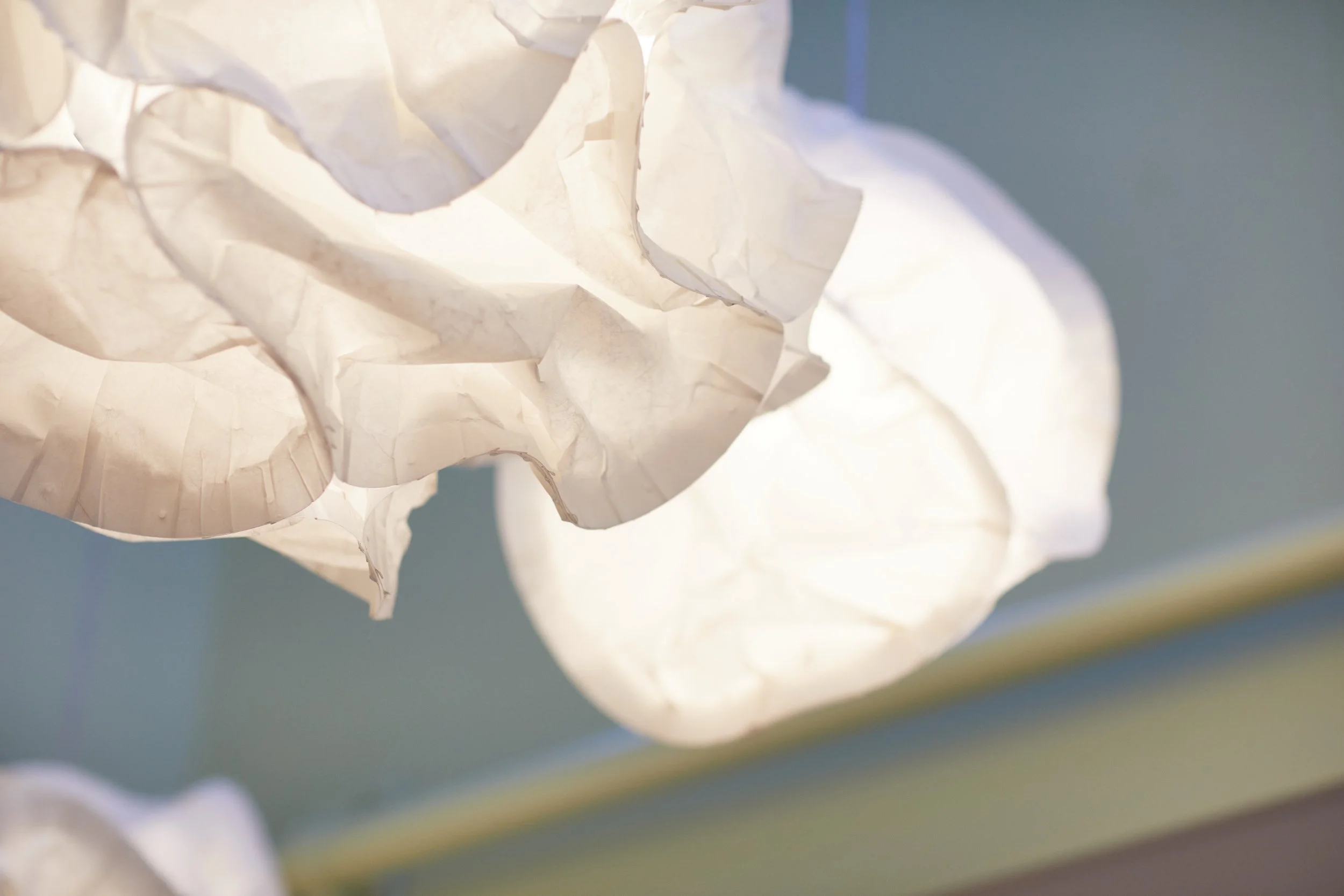 Lichtlampen gemaakt van wit papier in een artistiek design hangen tegen een blauwe muur.