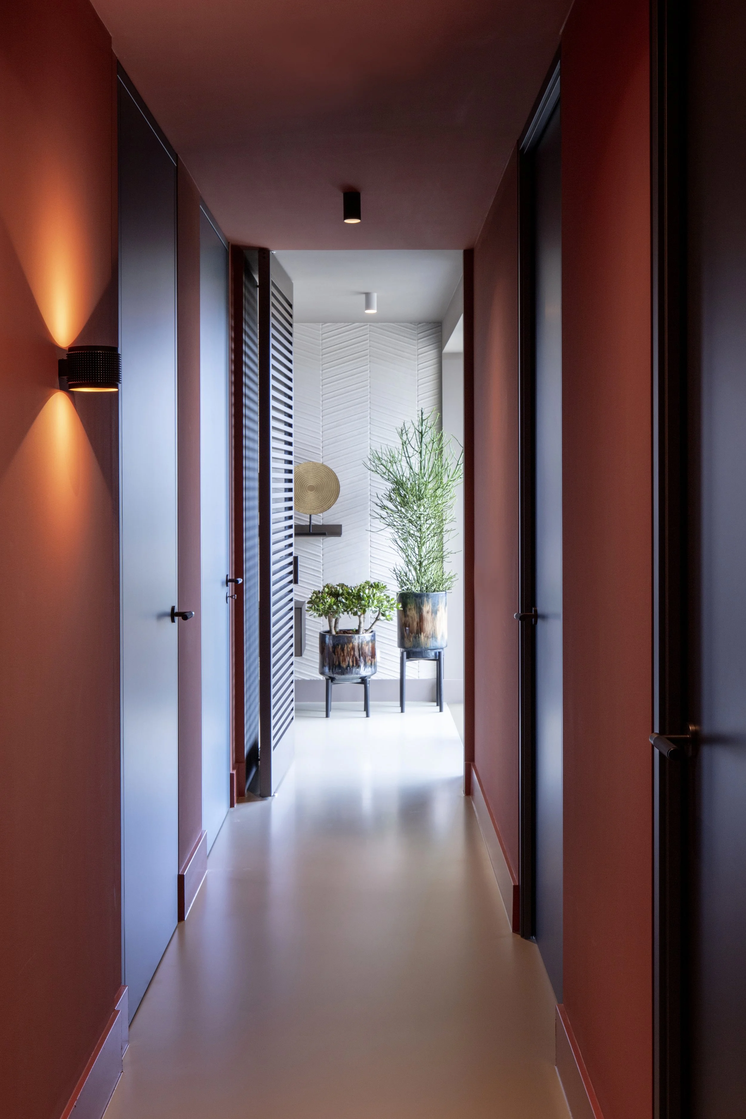 Moderne corridor met rode muren, zwarte en witte deuren, en groene planten in potten aan het einde.