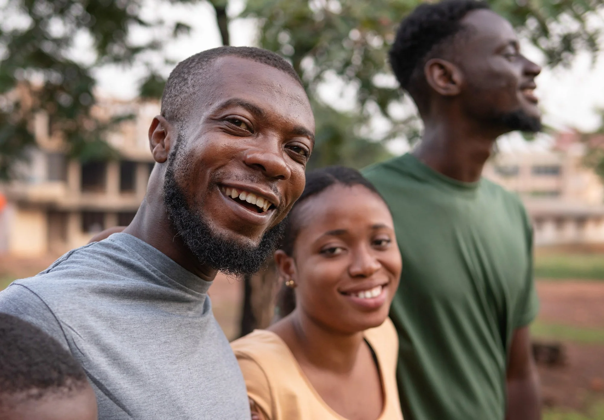 Close-up of smiling young African American man with a beard, other friends in the background outdoors.